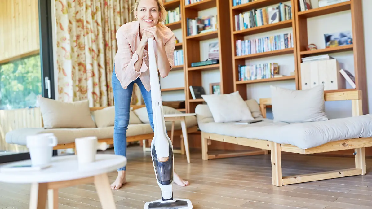 Blonde Frau stützt sich auf einem Akkusauger ab und schaut in die Kamera.