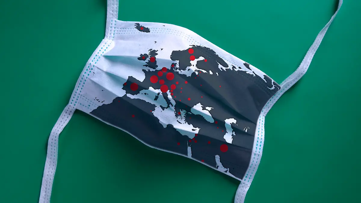 White face mask with a map of Europe is lying on a green background. The Covid-19 virus is rapidly spreading all over Europe.
