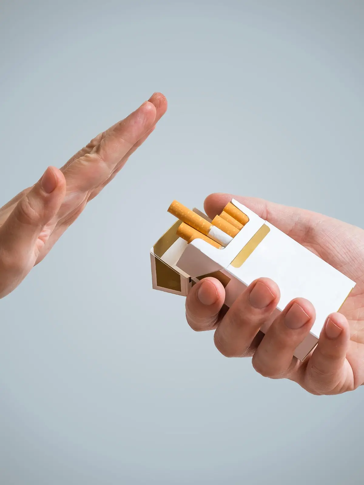 Man sieht zwei Hände vor einem grauen Hintergrund, die eine hält eine Packung Zigaretten in der Hand, die andere macht eine eindeutige Geste, diese abzulehnen.