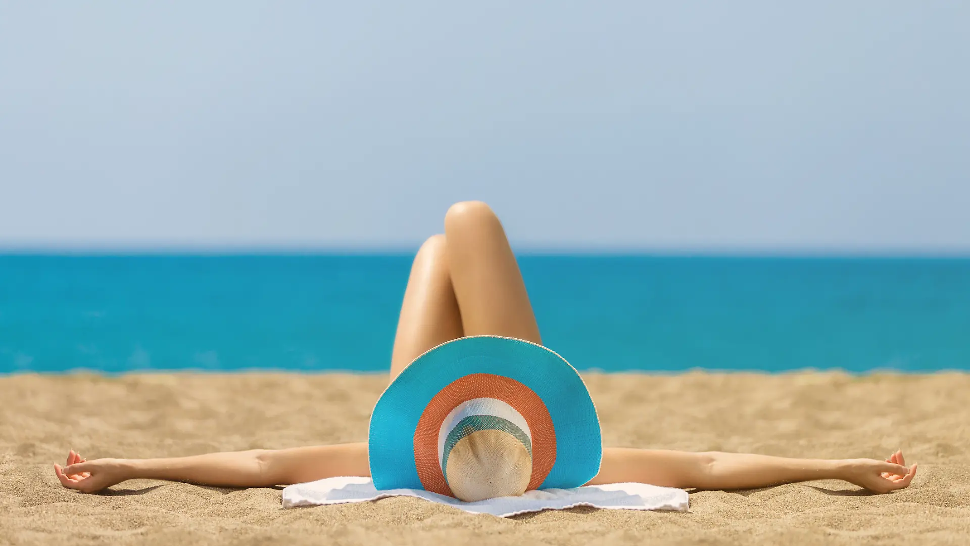 Frau mit Bikini und Hut liegt am Strand.