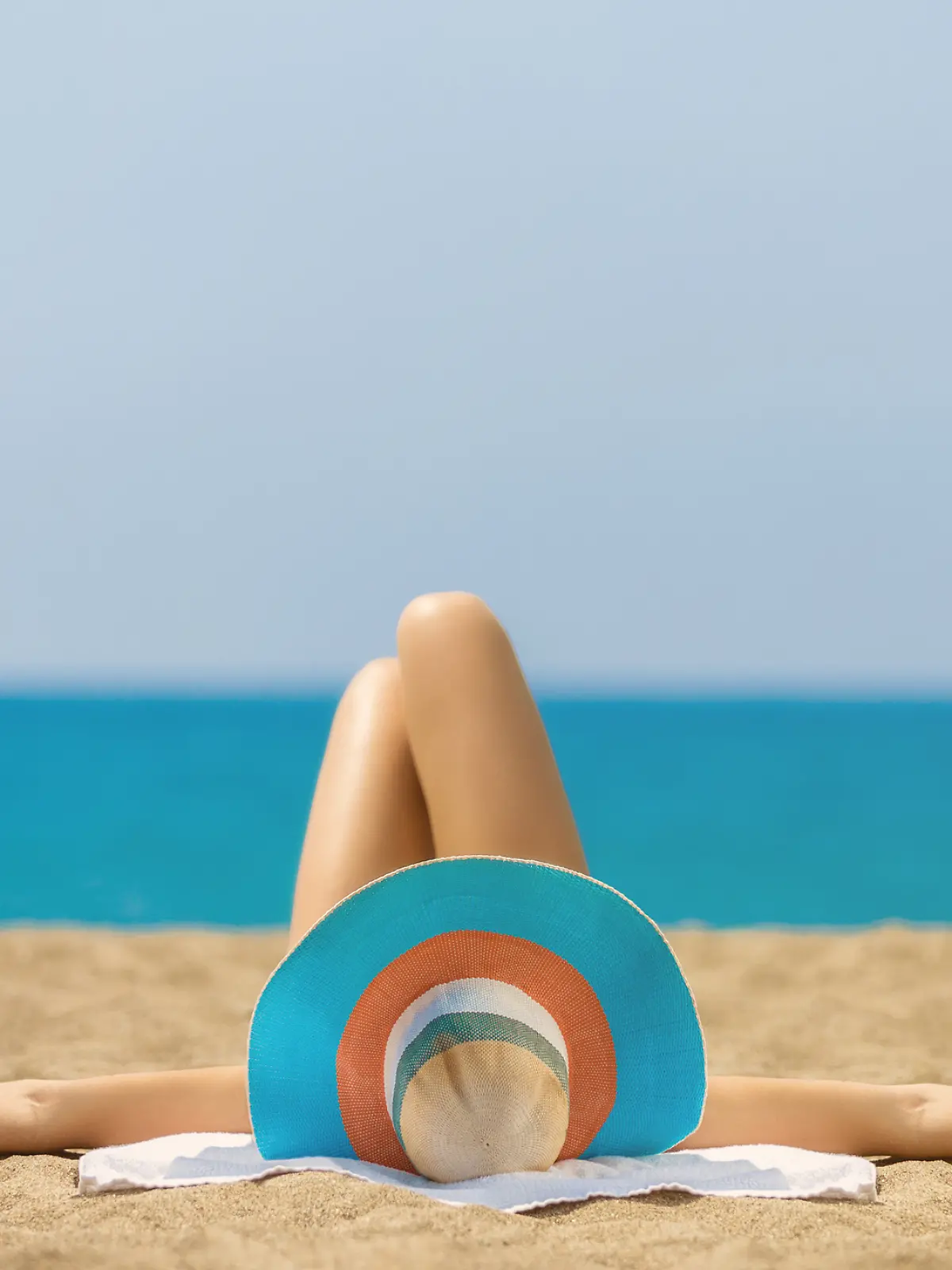 Frau mit Bikini und Hut liegt am Strand.
