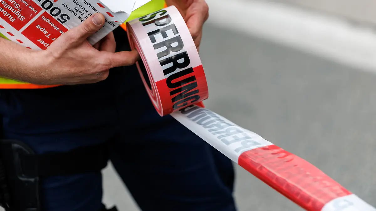 Ein Polizist rollt ein Flatterband mit der Aufschrift Polizeiabsperrung in Kiefersfelden (Bayern) von einer Rolle ab.