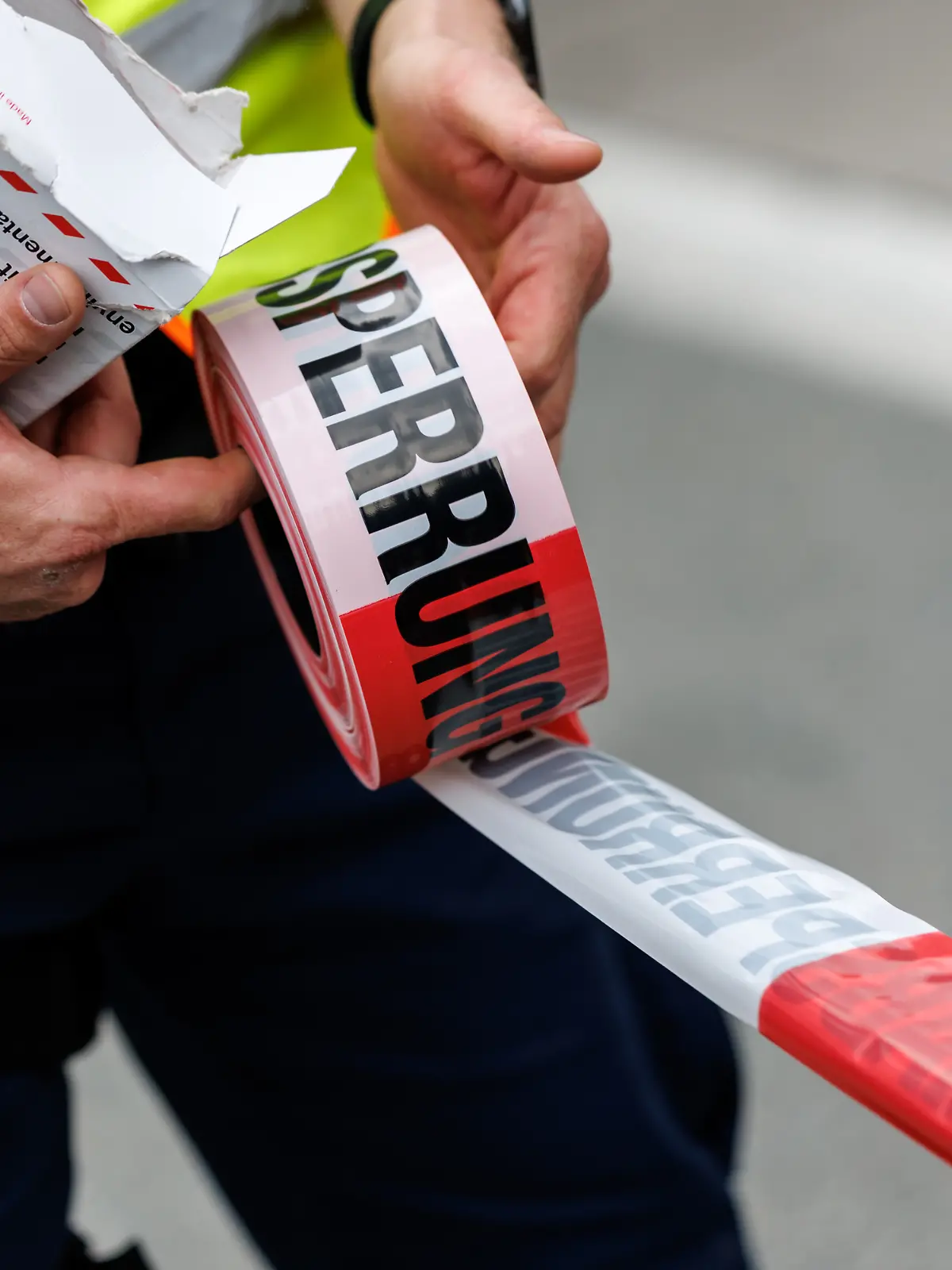 Ein Polizist rollt ein Flatterband mit der Aufschrift Polizeiabsperrung in Kiefersfelden (Bayern) von einer Rolle ab.