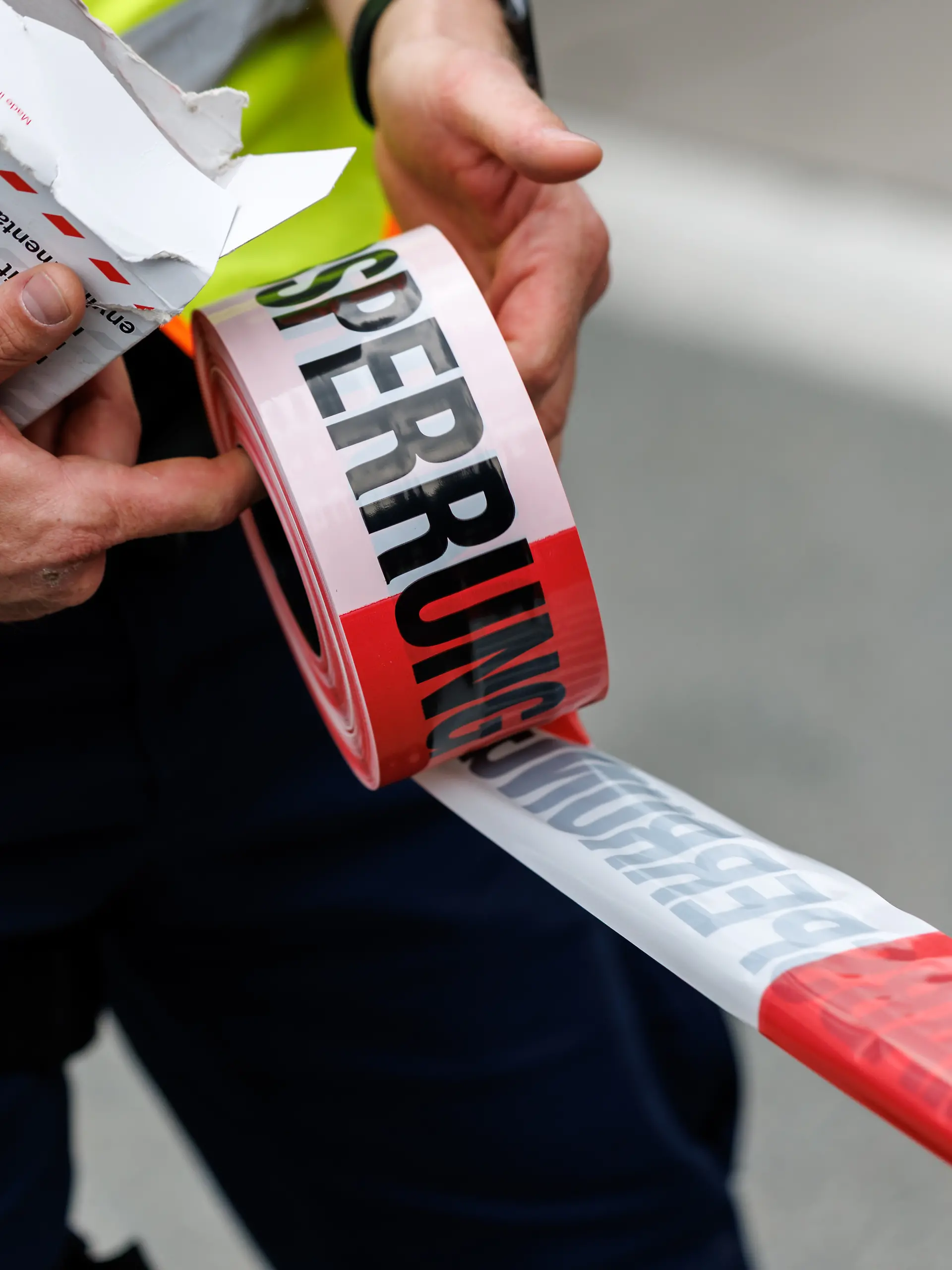 Ein Polizist rollt ein Flatterband mit der Aufschrift Polizeiabsperrung in Kiefersfelden (Bayern) von einer Rolle ab.