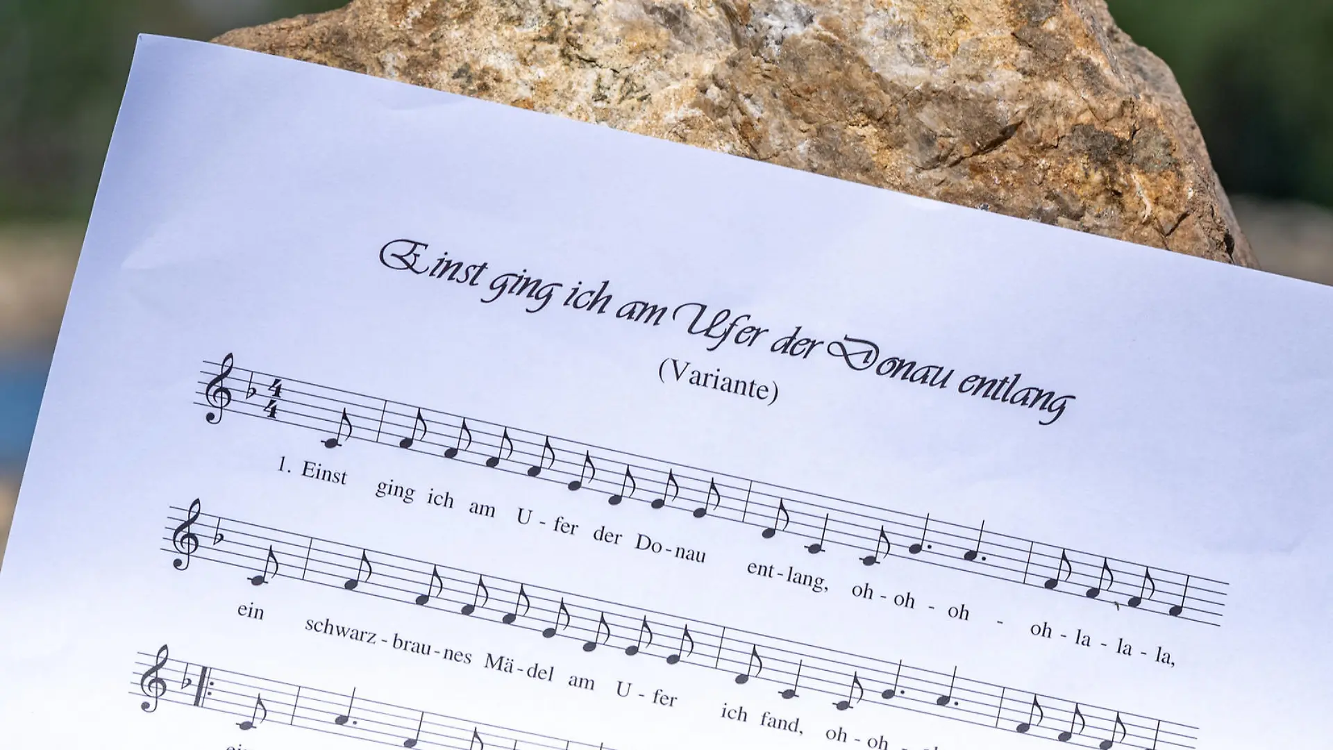 ILLUSTRATION - 28.05.2020, Bayern, Straubing: Ein Notenblatt mit dem Liedtext ·Einst ging ich am Ufer der Donau entlang· wird am Donauufer gehalten. In dem Lied wird die Vergewaltigung eines schlafenden Mädchens beschrieben. Foto: Armin Weigel/dpa +++ dpa-Bildfunk +++