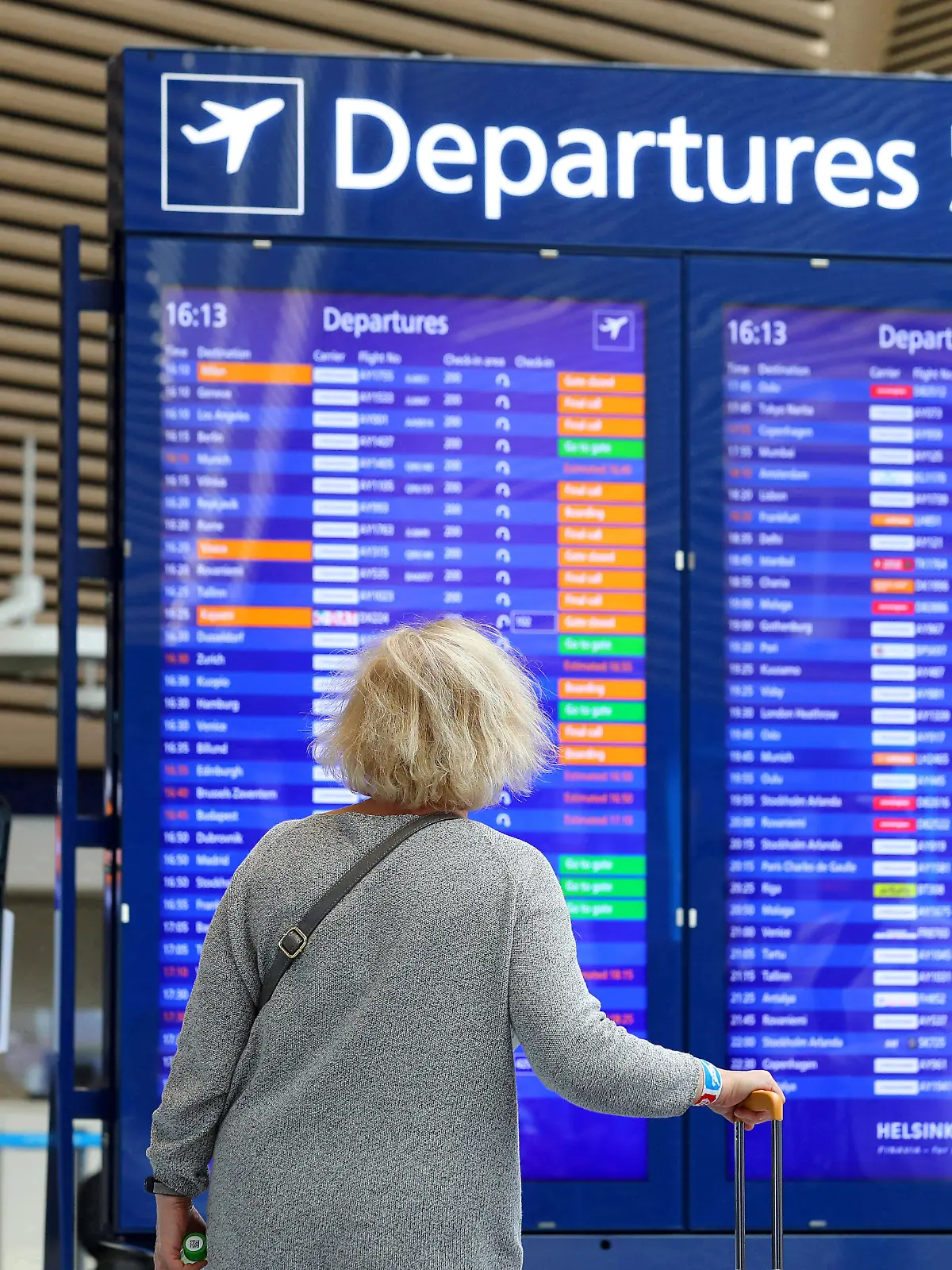 Eine Frau steht vor einer Anzeigetafel am Flughafen.
