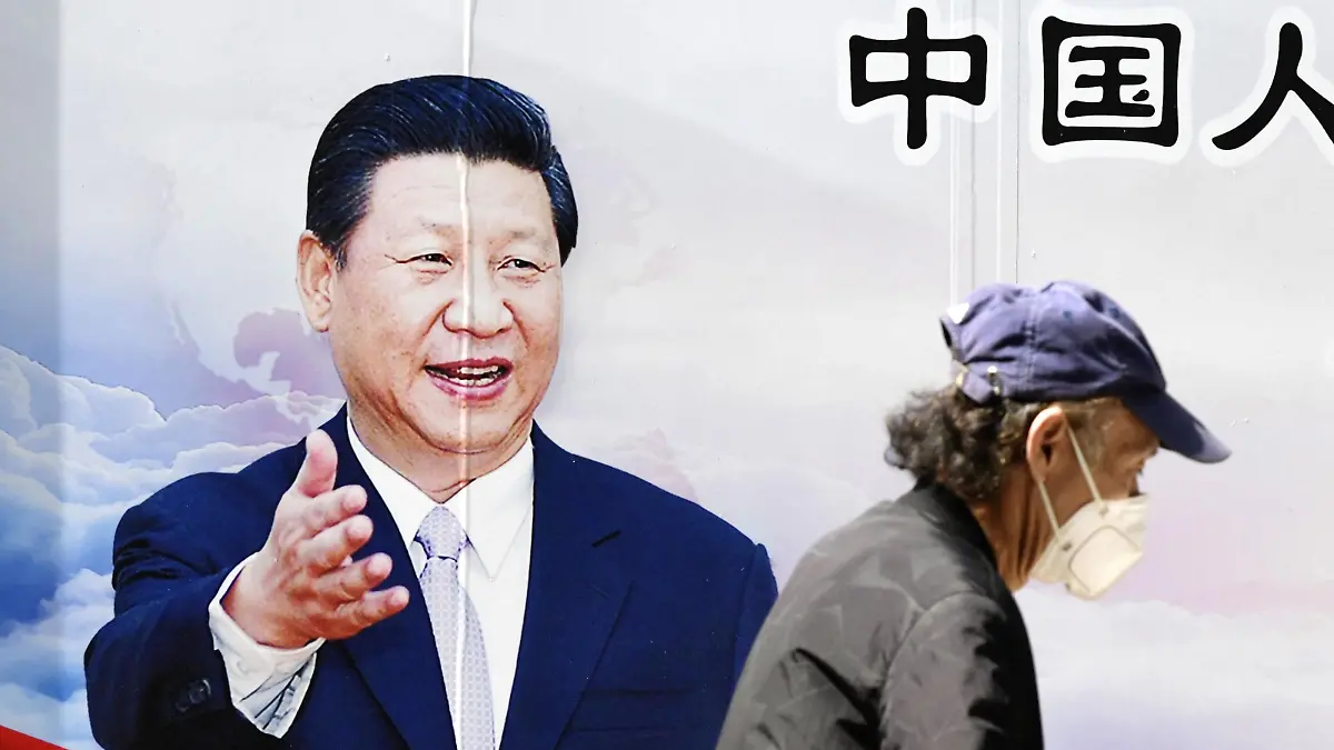 22.05.2020, China, Wuhan: Ein Mann spaziert mit einer Maske an einem Plakat von Chinas Präsident Xinping vorbei. Foto: -/kyodo/dpa +++ dpa-Bildfunk +++