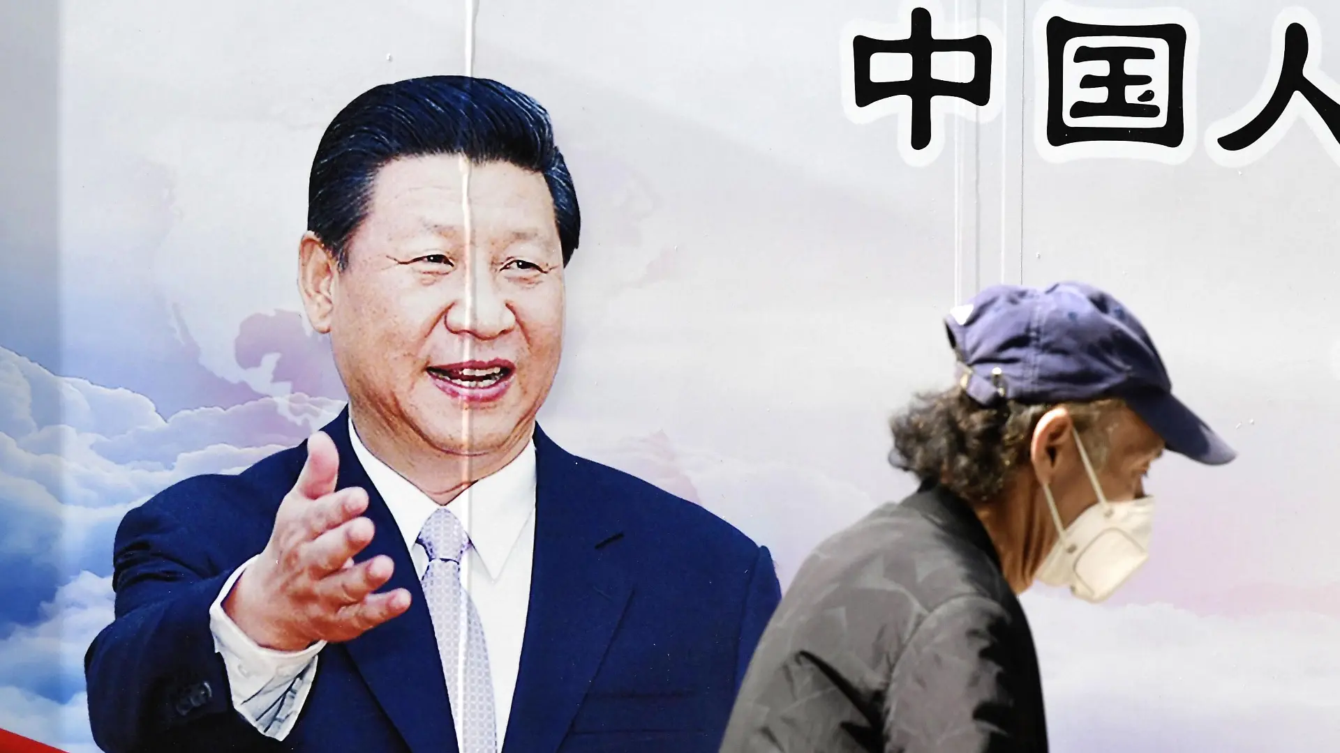 22.05.2020, China, Wuhan: Ein Mann spaziert mit einer Maske an einem Plakat von Chinas Präsident Xinping vorbei. Foto: -/kyodo/dpa +++ dpa-Bildfunk +++