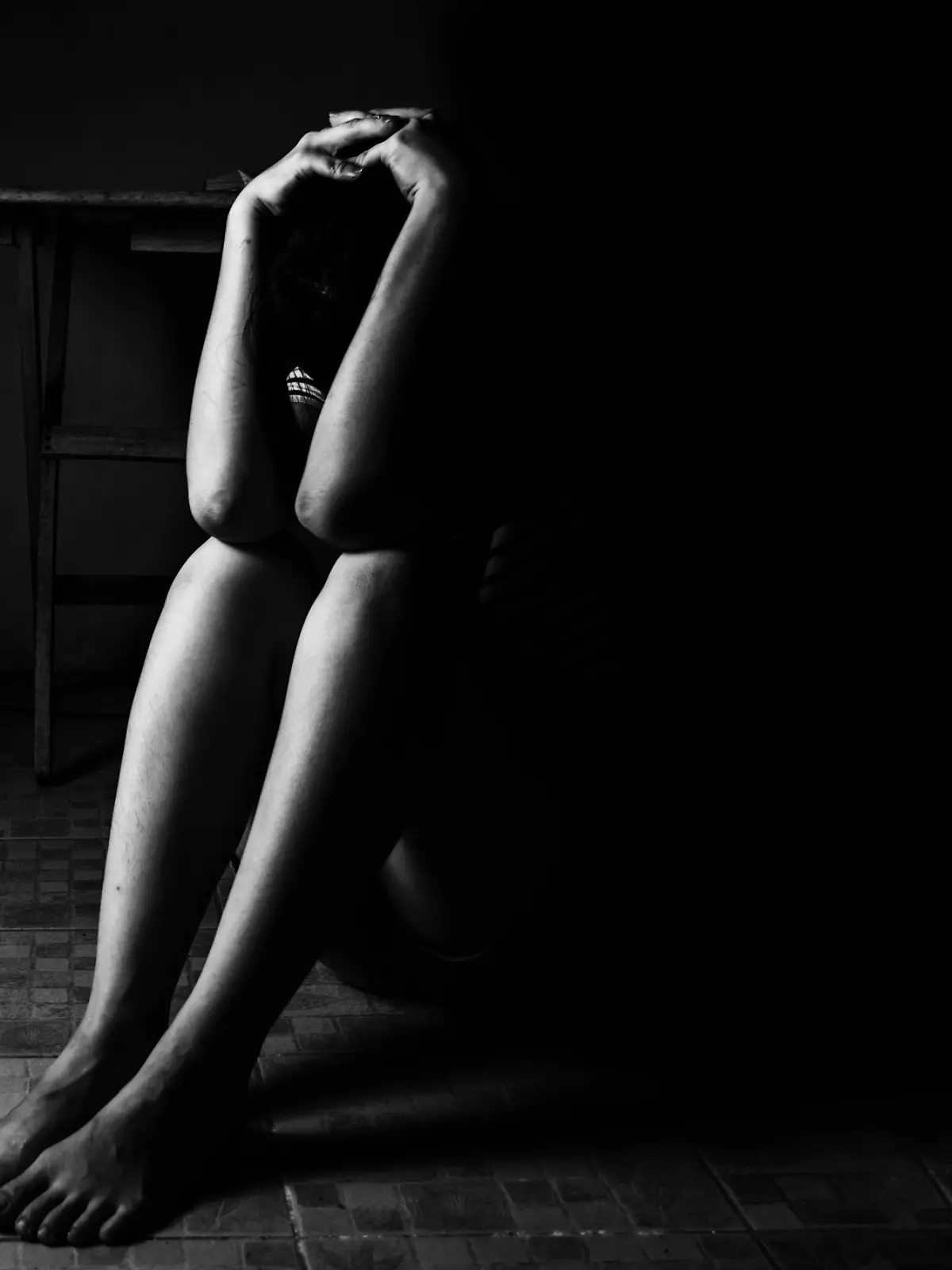 a woman sitting on ground with arm around lower head, sexual violence , sexual abuse, human trafficking concept with shadow edge in white tone