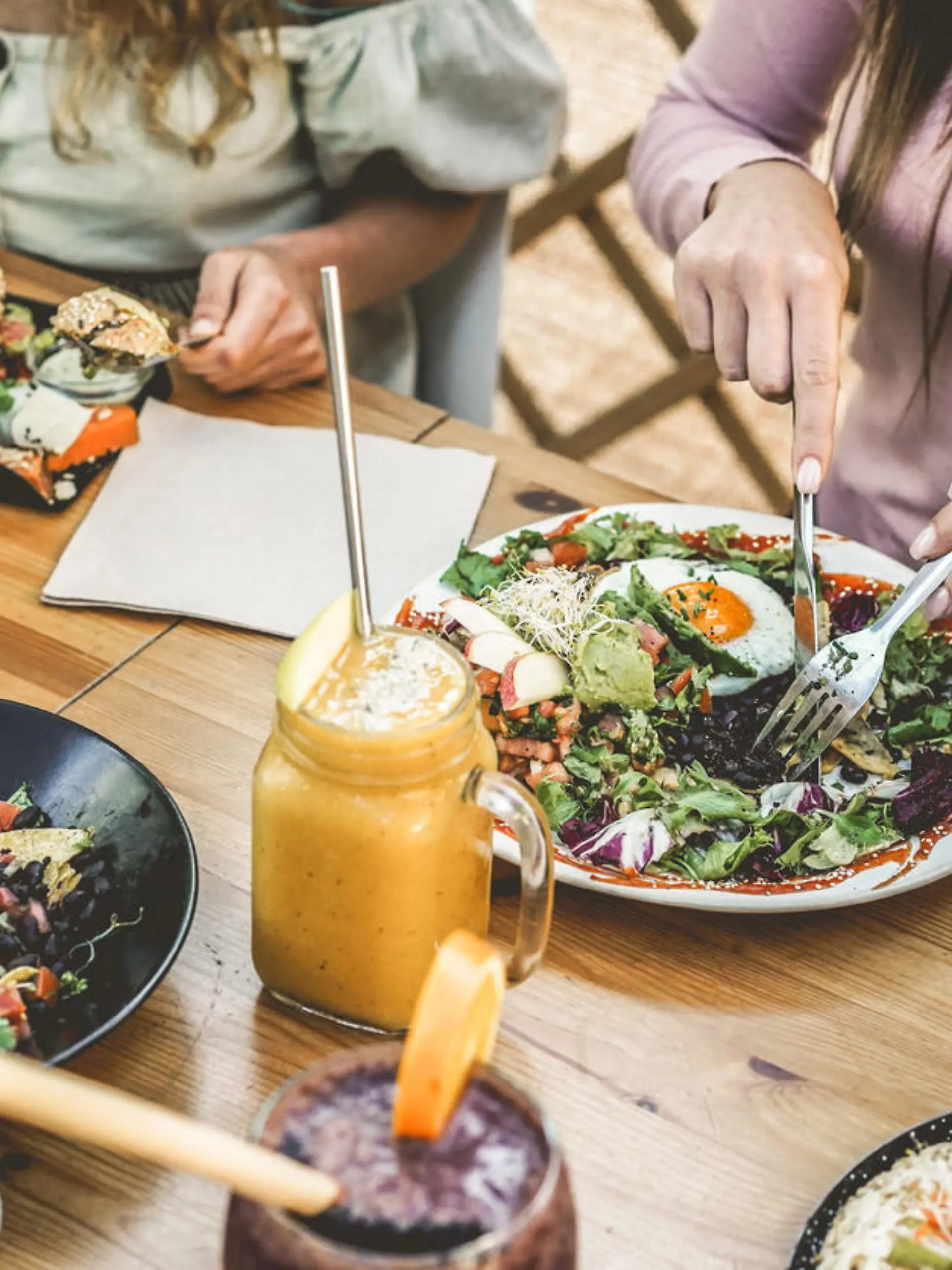 Hands view of young people eating brunch and drinking smoothies bowl with ecological straws in plastic free restaurant - Healthy lifestyle, food trends concept - Focus on top fork dish