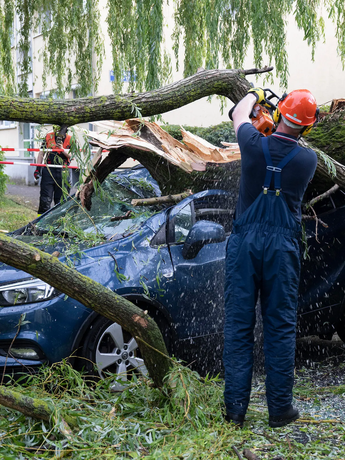 ARCHIV - 22.06.2023, Hessen, Frankfurt/Main: Nach einem schweren Unwetter räumen Feuerwehrleute Äste eines umgestürzten Baumes von einem geparkten Auto.     (zu dpa «Eine Woche nach dem Unwetter wird in Hessen weiter aufgeräumt») Foto: Boris Roessler/dpa +++ dpa-Bildfunk +++