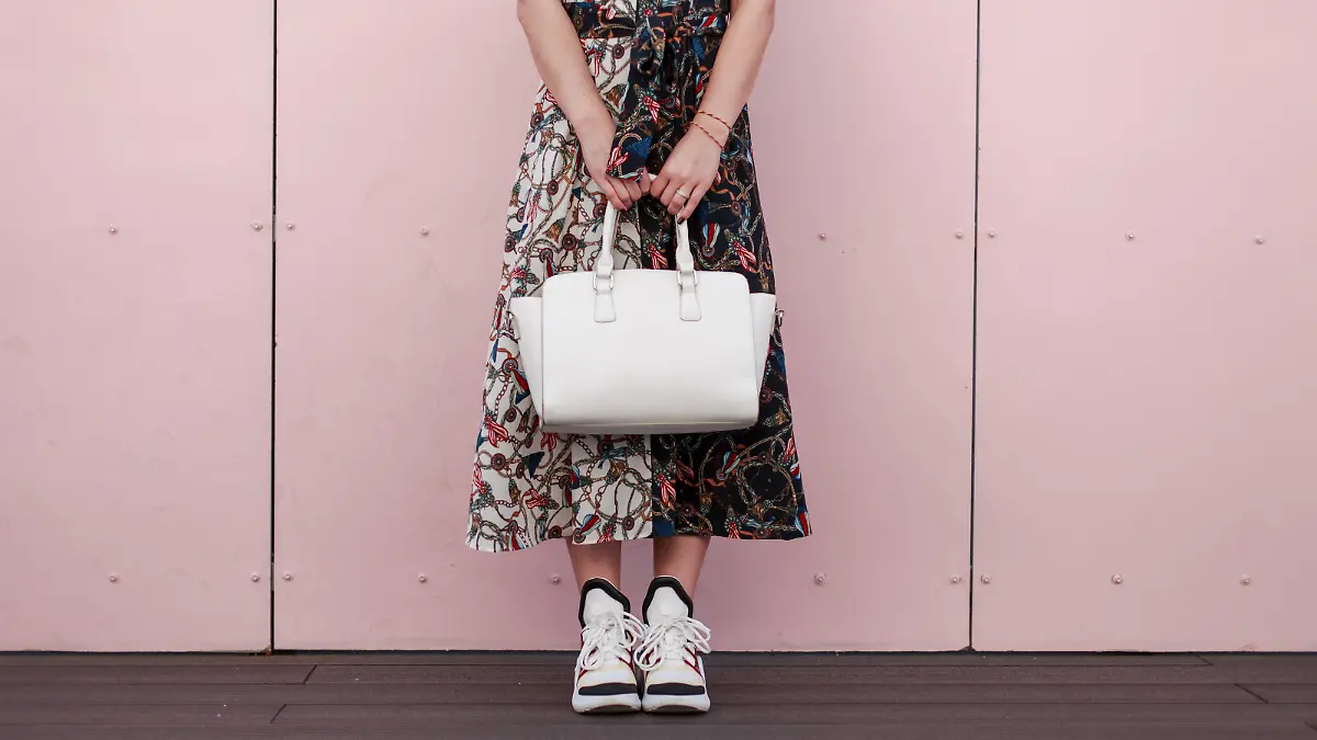 Woman in a fashionable dress with a white stylish bag stand near the pink wall. Women's Fashion Sneakers
