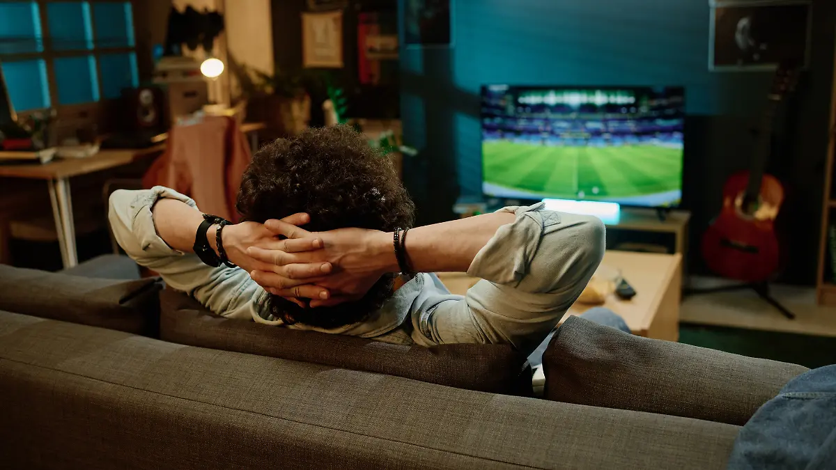 Ein Mann sitzt auf seiner Couch und schaut Fernsehen. Er streamt ein Fußballspiel.