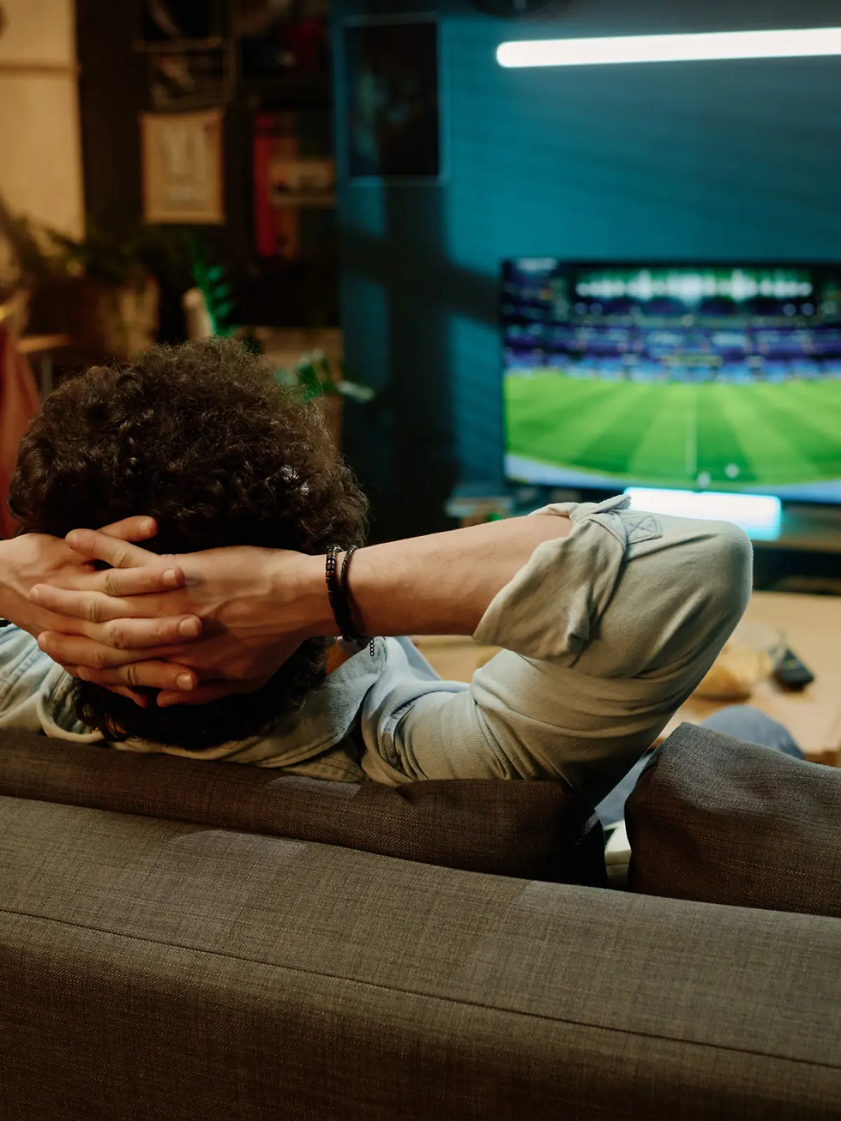 Ein Mann sitzt auf seiner Couch und schaut Fernsehen. Er streamt ein Fußballspiel.