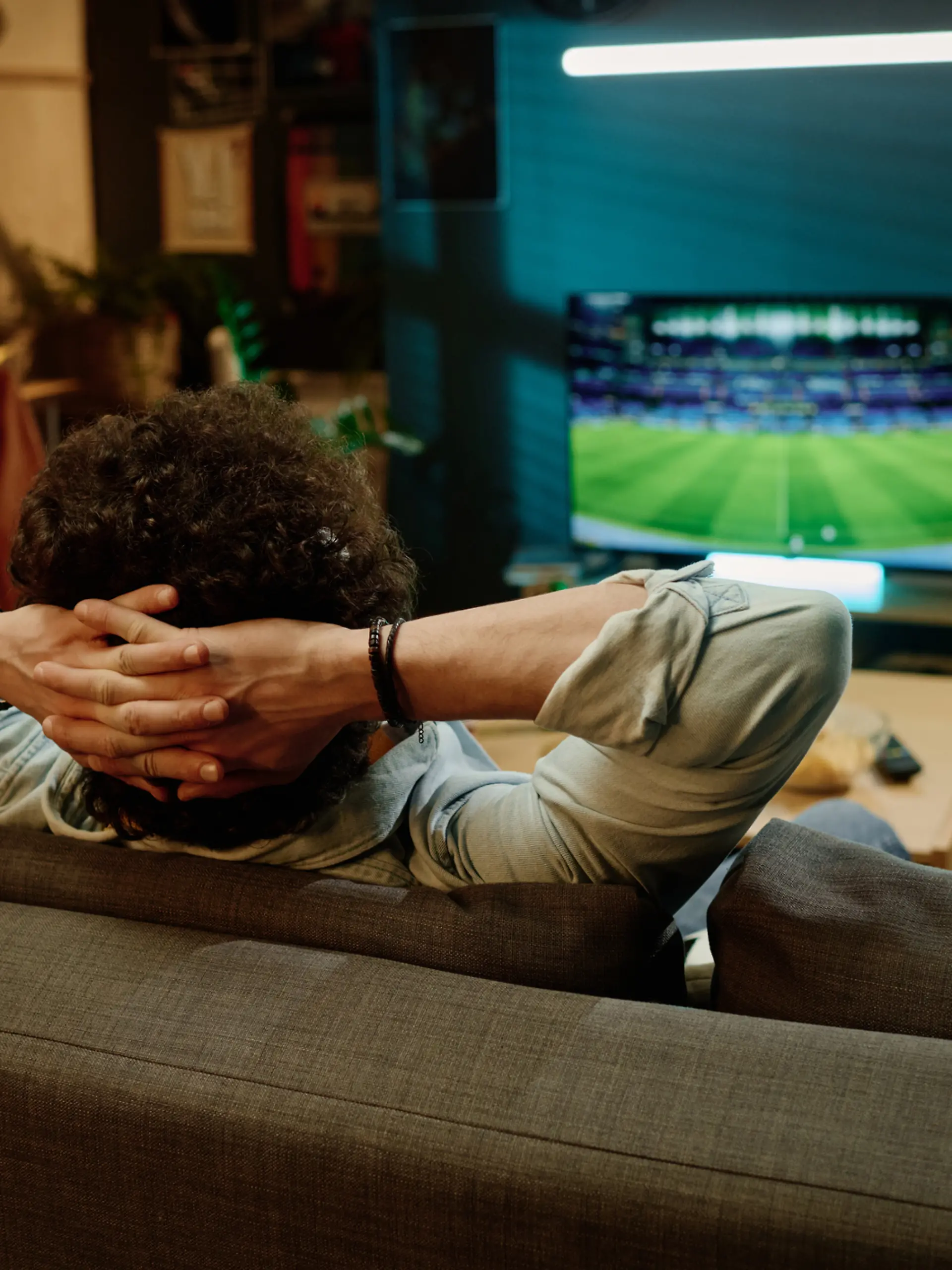 Ein Mann sitzt auf seiner Couch und schaut Fernsehen. Er streamt ein Fußballspiel.