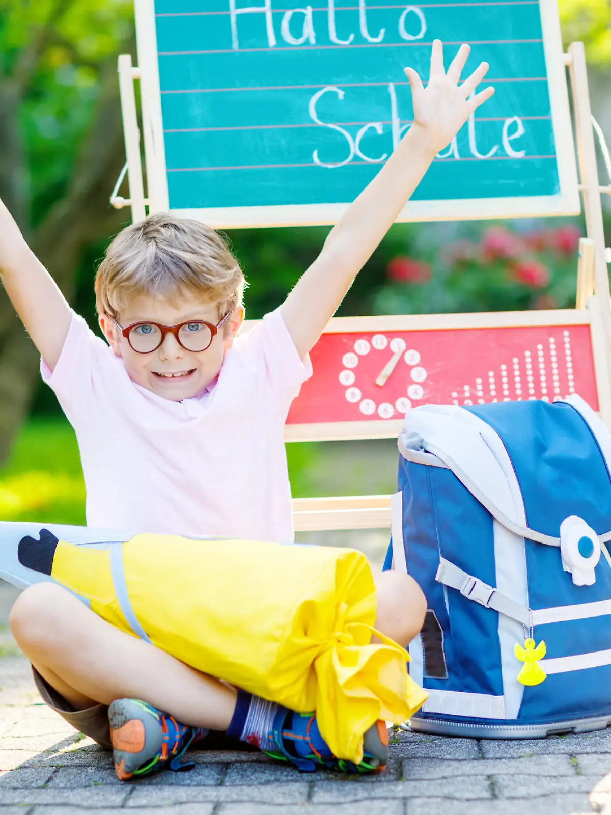 Happy little kid boy with glasses sitting by desk and backpack or satchel. Schoolkid with traditional German school bag called Schultuete on his first day to school. Hello school in German language