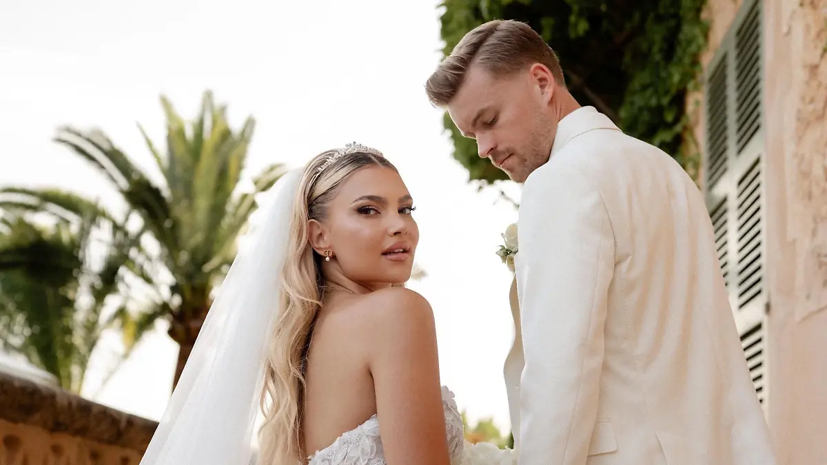 Hochzeitsfoto von Lea und Maximilian Mittelstädt: Beide stehen auf einer Treppe und schauen über ihre Schultern nach hinten - sie in einem weißen Brautkleid, der in einem weißen Anzug