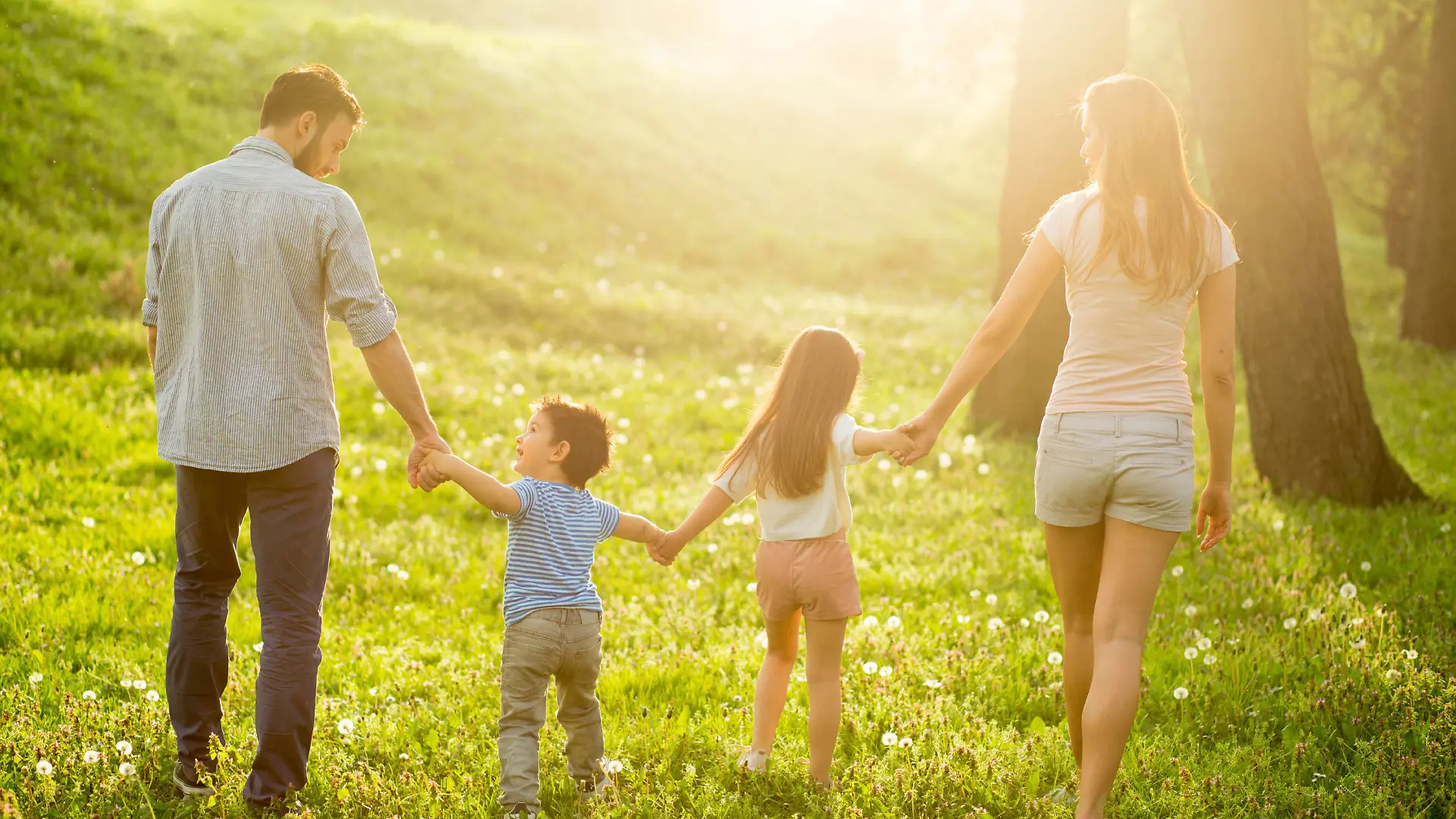 Young smiling parents holding hands and walking with their children in nature
