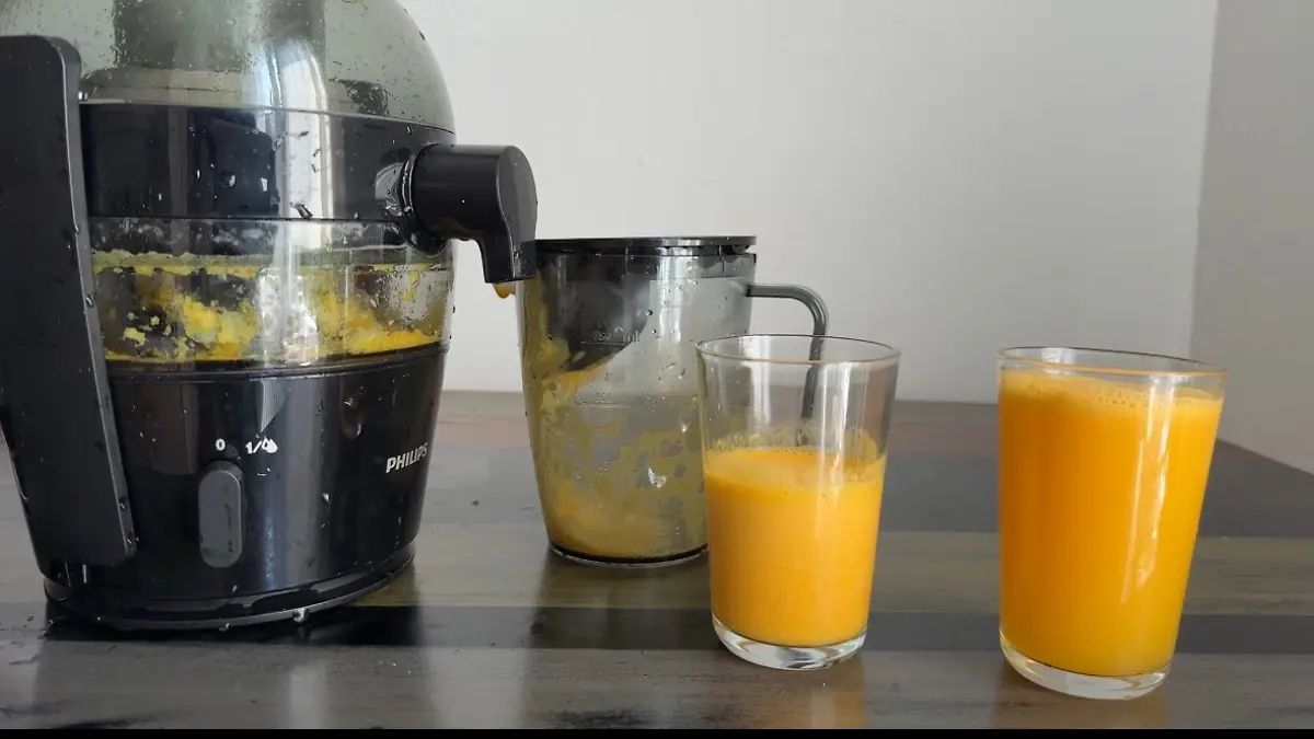 Zwei Gläser mit frisch gepresstem Orangensaft vor dem Philips-Entsafter mit sichtbarem Tresterbehälter