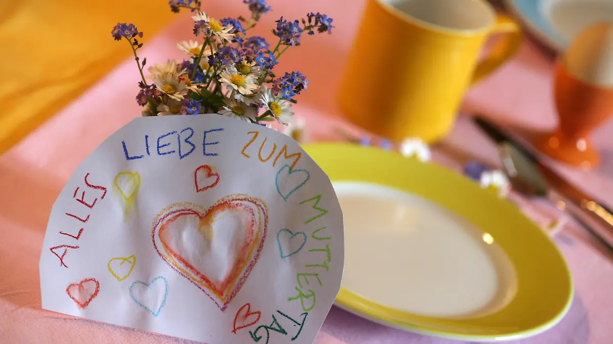 ARCHIV - 07.05.2017, Bayern, Kaufbeuren: An einem Strauß Blumen auf einem gedeckten Frühstückstisch lehnt ein Papier mit der Aufschrift «Alles Liebe zum Muttertag». (Zu dpa "Rollentausch und Erschöpfung: Mütter in der Corona-Krise") Foto: Karl-Josef Hildenbrand/dpa +++ dpa-Bildfunk +++