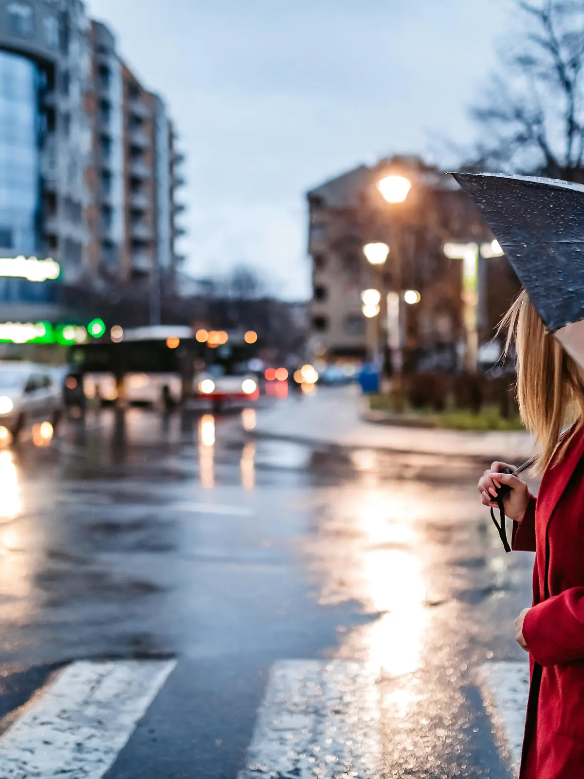 Young Caucasian smiling woman crossing street downtown in rain with umbrella. Autumn time.