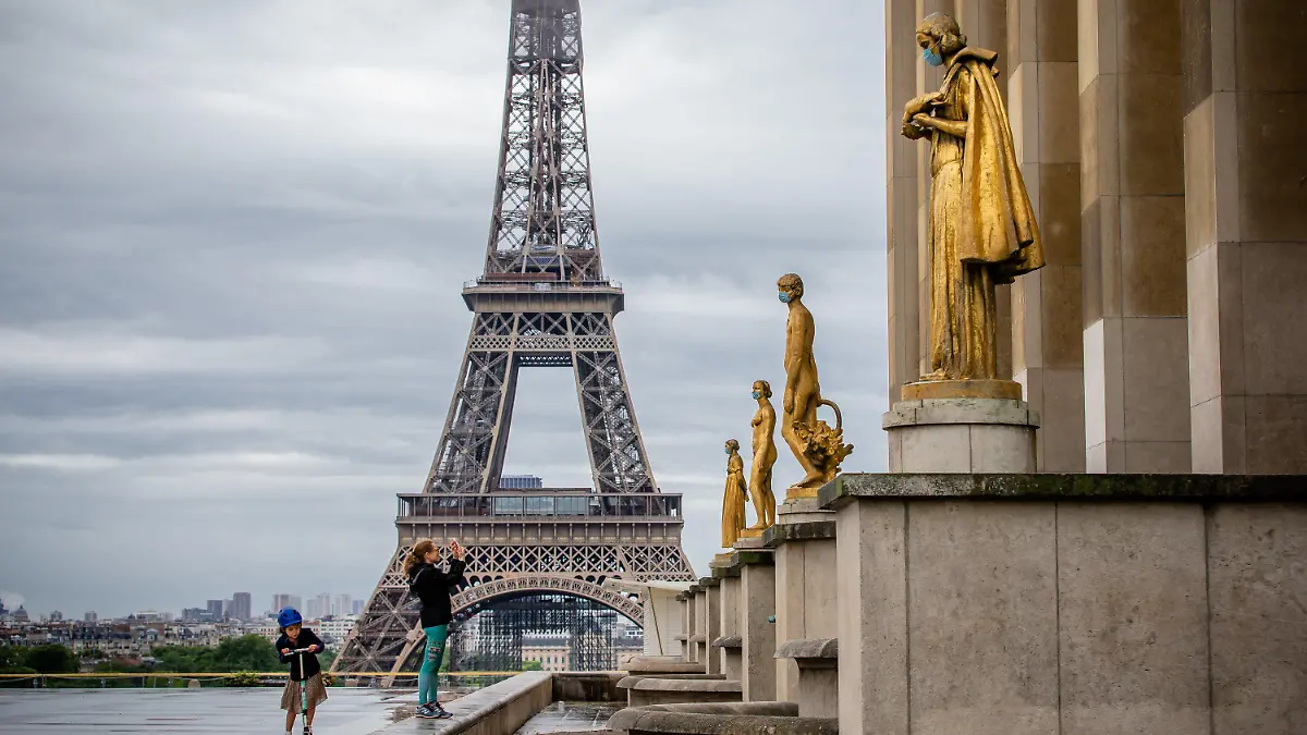 03.05.2020, Frankreich, Paris: Ein Mädchen fotografiert Bronzestatuen mit Mundschutz auf dem Parvis des Droits de l'Homme (Place du Trocadéro) mit Blick auf den Eiffelturm. Die französische Regierung hat beschlossen, den Ausnahmezustand bis zum 24. Juli zu verlängern, um das Coronavirus zu bekämpfen, kündigte Gesundheitsminister Vrran an. Foto: Aurelien Morissard/XinHua/dpa +++ dpa-Bildfunk +++