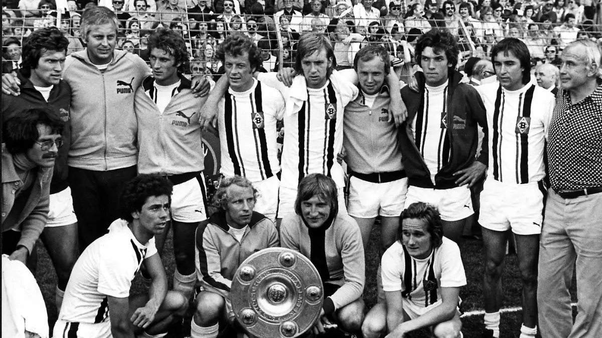 ARCHIV - 07.06.1975, Nordrhein-Westfalen, Mönchengladbach: Gruppenbild des Deutschen Meisters Borussia Mönchengladbach nach dem Sieg am vorletzten Spieltag der Bundesliga gegen Eintracht Braunschweig in Mönchengladbach. (Stehend v.l.n.r) Jupp Heynckes, Trainerassistent Karl-Heinz Drygalski, Rainer Bonhof, Wimmer, Jensen, Wittkamp, Schäffer, Danner und «Meistermacher» Trainer Hennes Weisweiler. (Vorn v.l.n.r) Masseur Stock, Klinkhammer, Berti Vogts, Kleff und Alan Simonsen. (zu "Keine große Bühne mehr: Heynckes sinniert zum 75. über Gesellschaft") Foto: Scheidemann/dpa +++ dpa-Bildfunk +++