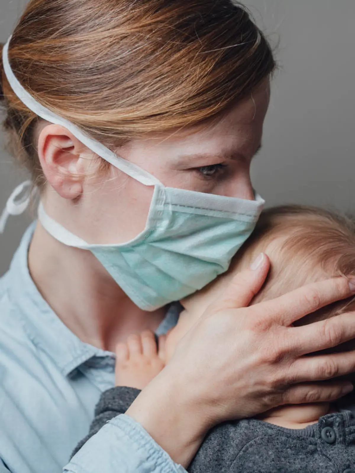 Krankenschwester mit Mundschutz trägt Kleinkind
