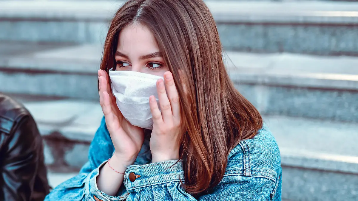 Frau mit Maske fasst sich ins Gesicht