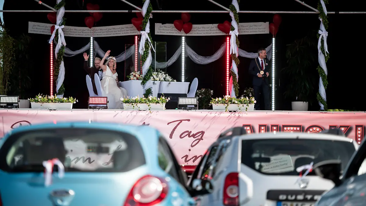 05.05.2020, Nordrhein-Westfalen, Düsseldorf: Das Brautpaar Janine und Philip Scholz (l) sitzt mit Düsseldorfs Oberbürgermeister Thomas Geisel (SPD) bei ihrer Trauung im Autokino auf der Bühne. Drei Paare geben sich im Autokino das Ja-Wort. Ihre Gäste können die Trauung über das Autoradio mithören. Das Paar heiratete ganz in rot-weiß · zu Ehren des 125. Jubiläums des Fußballclubs Fortuna Düsseldorf. Foto: Fabian Strauch/dpa +++ dpa-Bildfunk +++