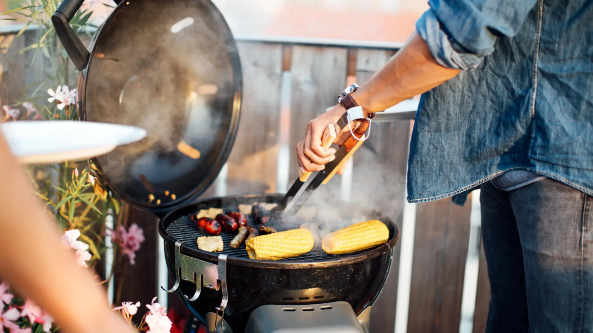 Mann grillt auf einem Balkon.