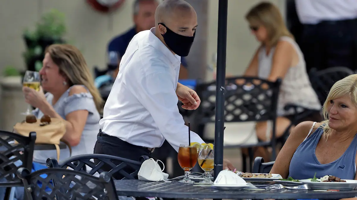 A foodserver at the Parkshore Grill restaurant wears a protective face mask as he waits on customers Monday, May 4, 2020, in St. Petersburg, Fla. Several restaurants are reopening with a 25% capacity as part of Florida Gov. Ron DeSantis' plan to stop the spread of the coronavirus. (AP Photo/Chris O'Meara)