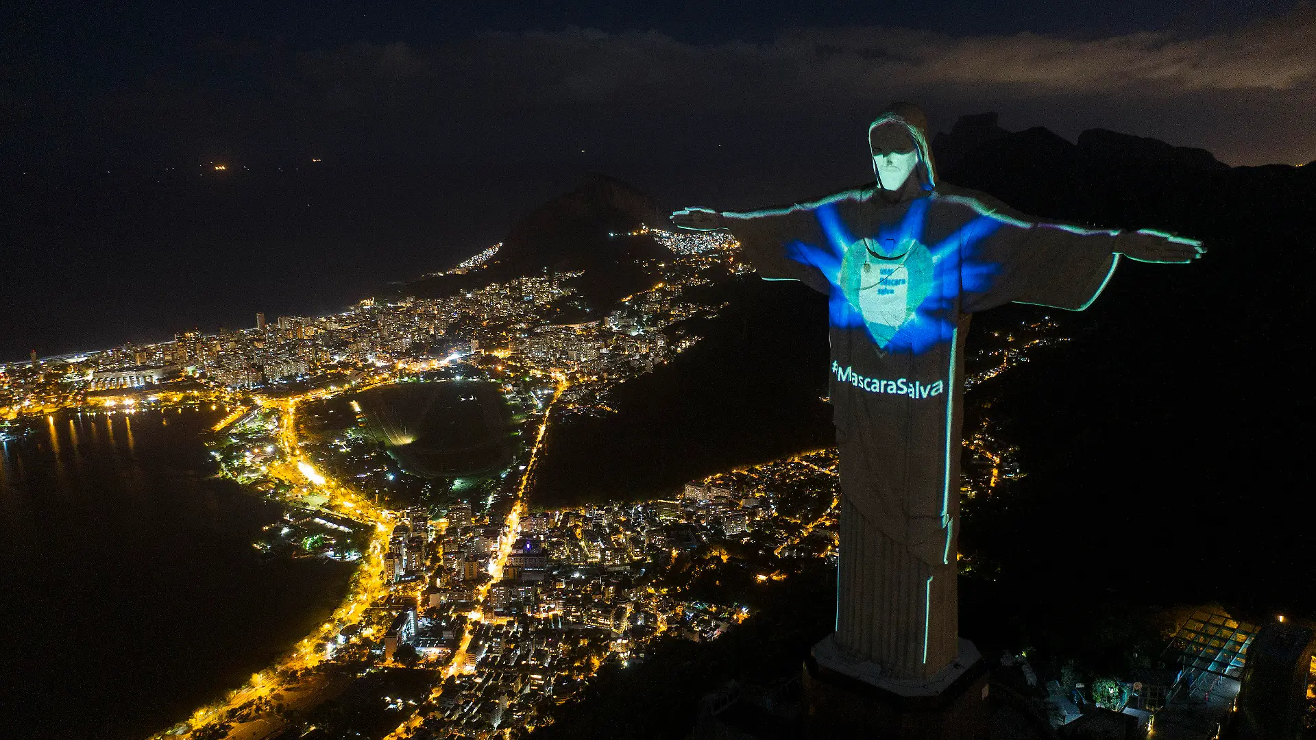04.05.2020, Brasilien, Rio de Janeiro: Die Christus-Erlöser-Statue in Rio ist beleuchtet, als ob sie eine Mundschutzmaske tragen würde. «Die Maske rettet» ist auf Portugiesisch zu lesen. In Brasilien haben sich nach offiziellen Angaben nun mehr als 100 000 Menschen mit dem neuartigen Coronavirus infiziert. Foto: Leo Correa/AP/dpa +++ dpa-Bildfunk +++