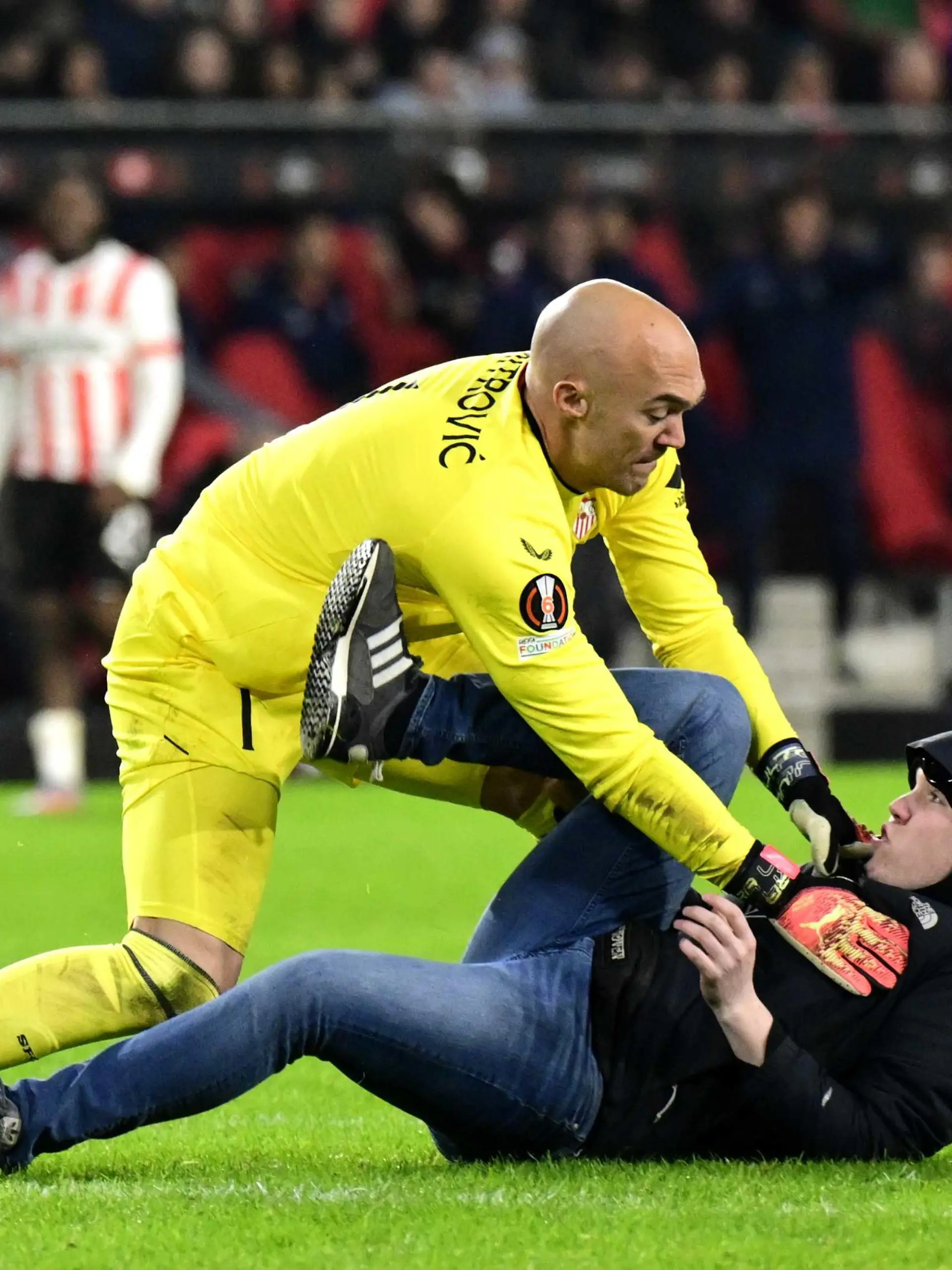 ARCHIV - 23.02.2023, Niederlande, Eindhoven: Fußball: Europa League, PSV Eindhoven - FC Sevilla, K.o.-Runde, Zwischenrunde, Rückspiele: Ein PSV-Fan (r) greift Sevilla FC-Torhüter Marko Dmitrovic im Phillips-Stadion während des Spiels an. Der Angreifer wurde nun verurteilt. (zu dpa: «Haftstrafe für Eindhoven-Fan nach Attacke auf Sevilla-Torwart») Foto: Olaf Kraak/ANP/dpa +++ dpa-Bildfunk +++