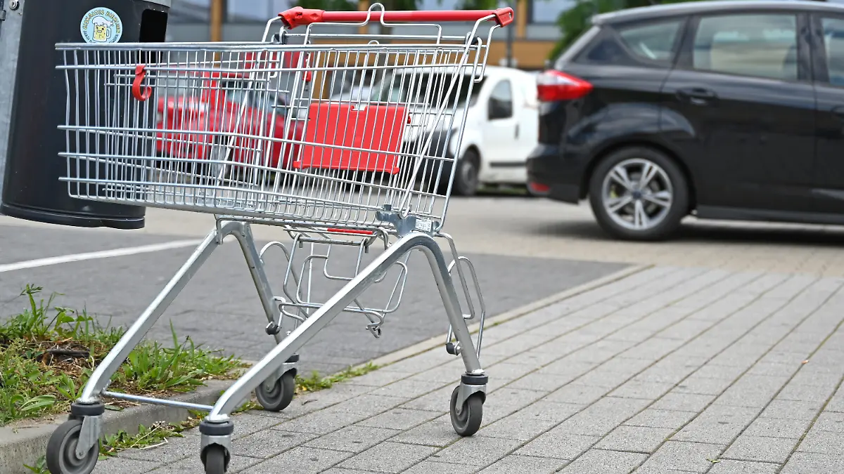 Ein leerer Einkaufswagen steht auf einem Parkplatz vor einem Supermarkt.