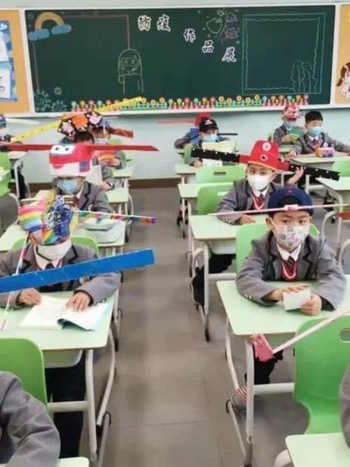 Chinesische Grundschüler tragen lustige Hüte als Corona-Abstandhalter.