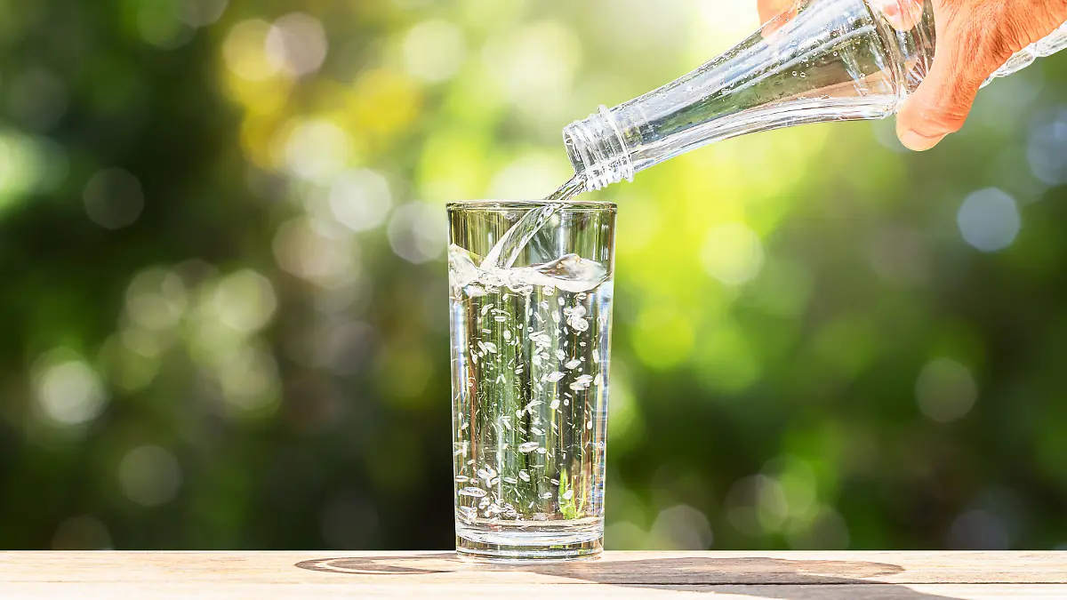 Männliche Hand gießt Wasser aus einer Glasflasche in ein Glas.