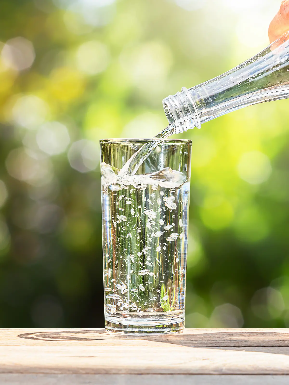 Männliche Hand gießt Wasser aus einer Glasflasche in ein Glas.