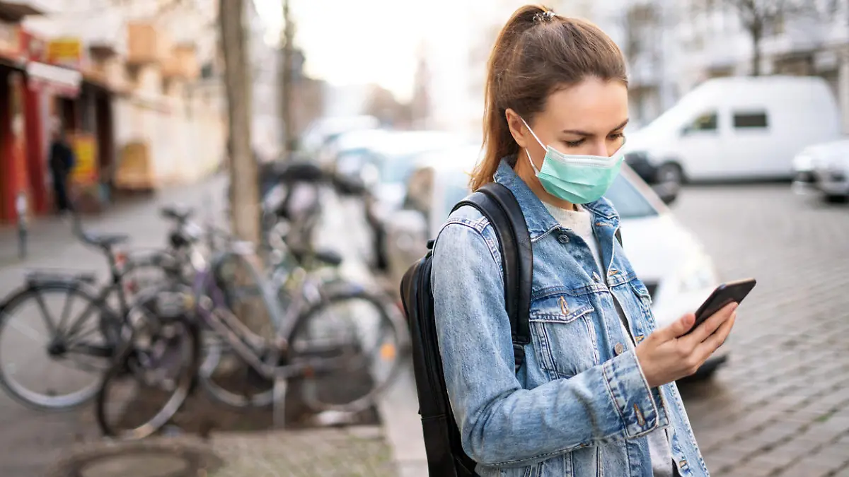 Junge Frau mit Mund-Nasen-Maske schaut auf ihr Smartphone