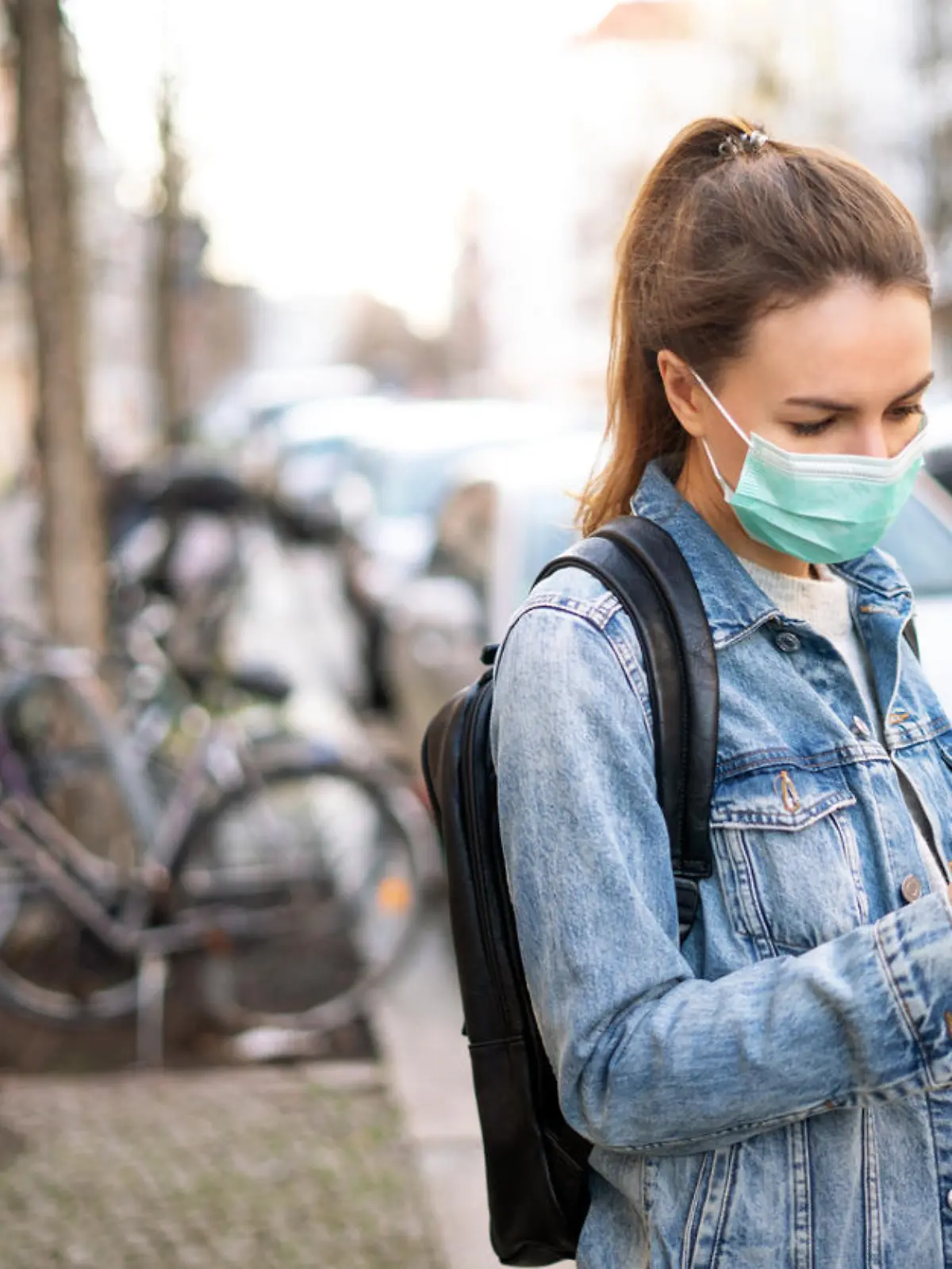 Junge Frau mit Mund-Nasen-Maske schaut auf ihr Smartphone