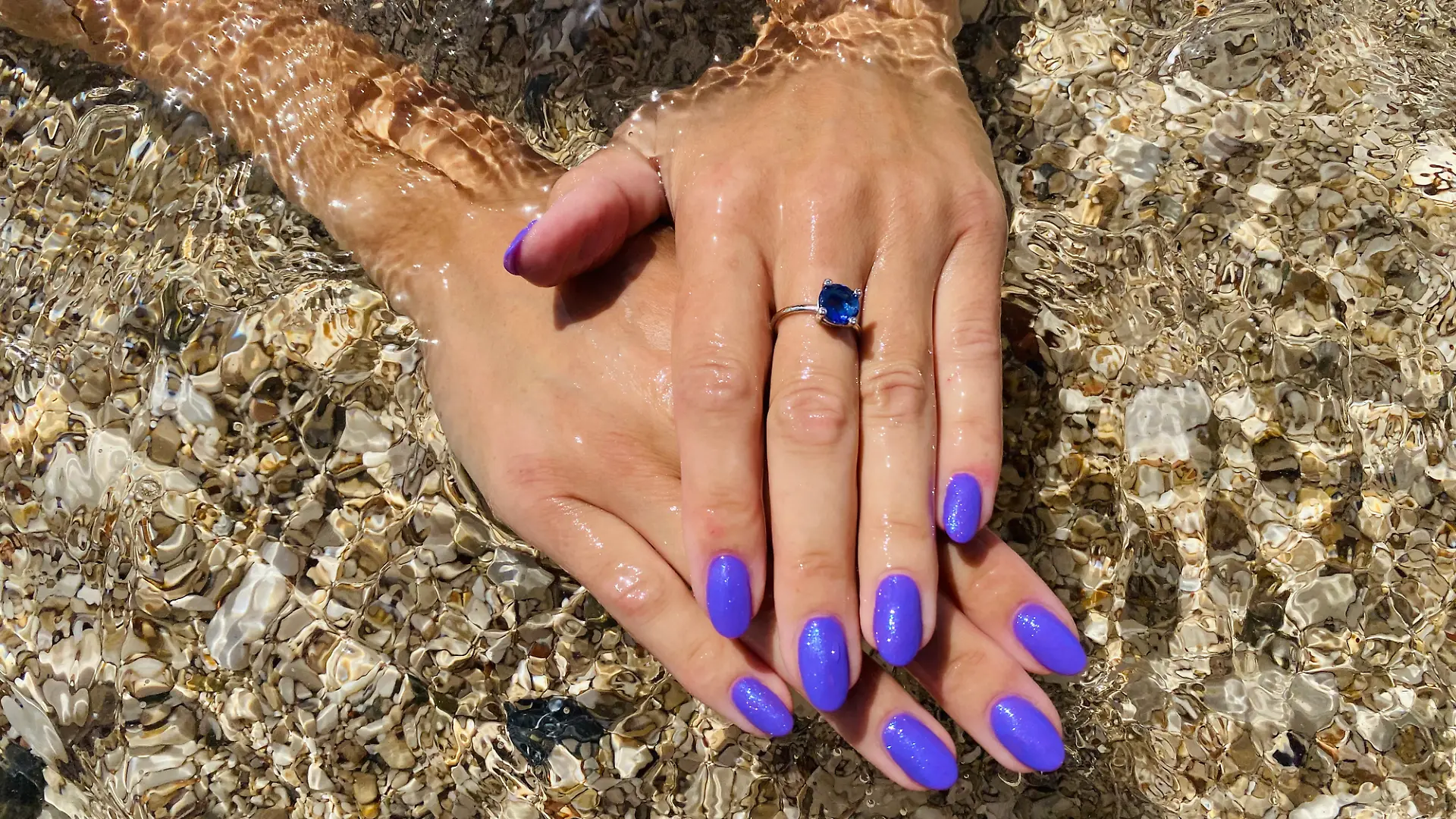 Eine Frau hält ihre perfekt manikürten Fingernägel ins Meerwasser.