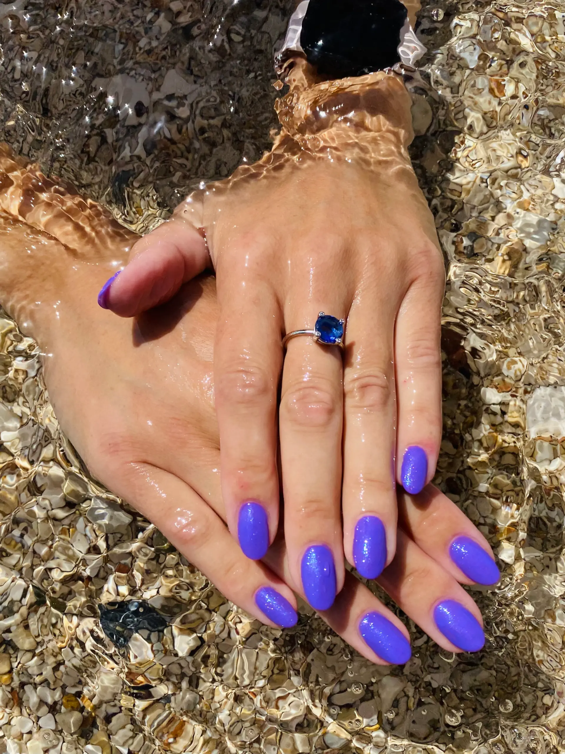 Eine Frau hält ihre perfekt manikürten Fingernägel ins Meerwasser.