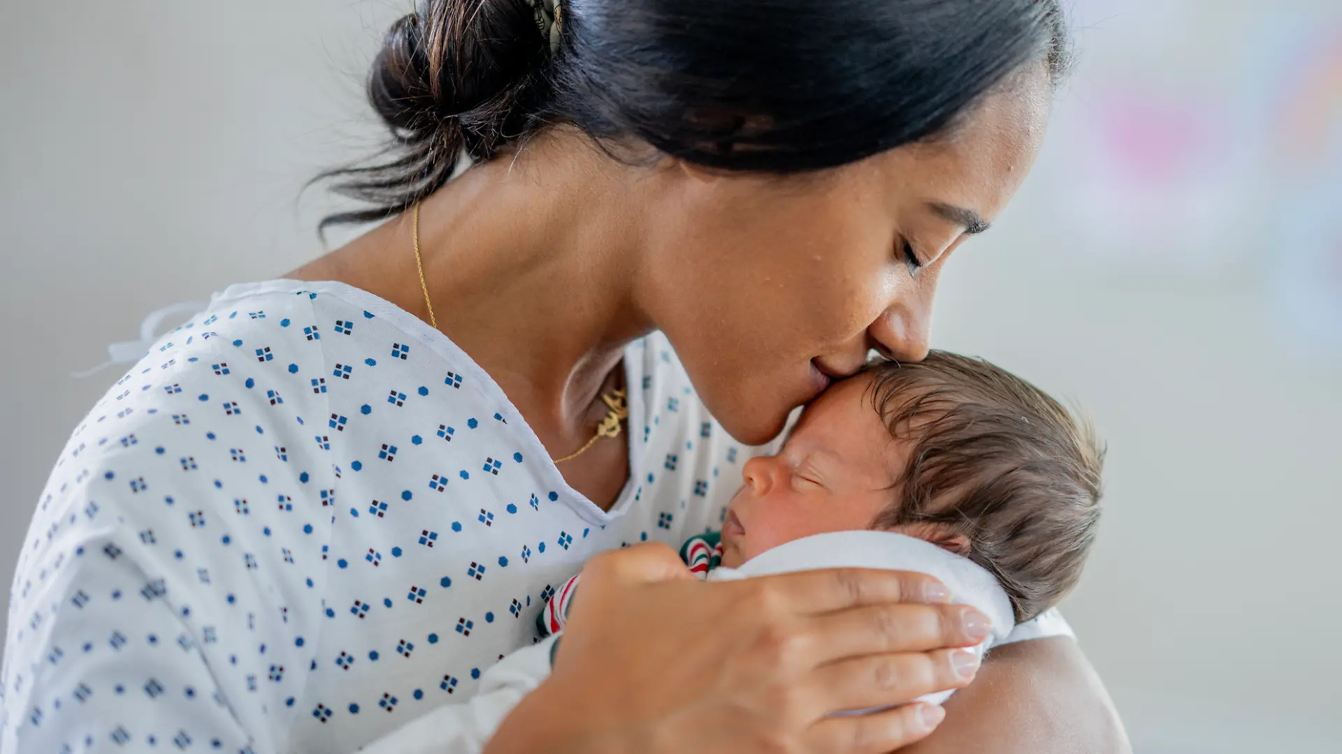 Eine Mutter küsst ihr Neugeborenes / Baby.