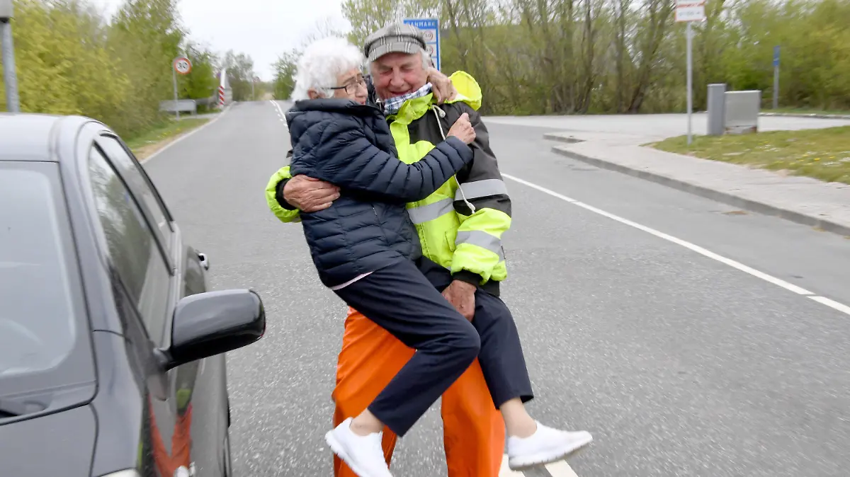 24.04.2020, Schleswig-Holstein, Aventoft: Inga Rasmussen aus Dänemark (85) wird von Karsten Tüchsen Hansen (89) aus Nordfriesland bei ihrem täglchen Treffen an der deutsch-dänischen Grenze hochgehoben. Nach Schließung der Grenze am 14.03.2020 hatten sich die beiden täglich am Schlagbaum getroffen. Jetzt hat Dänemark die Regelung zur Freude des Paares gelockert. Foto: Carsten Rehder/dpa +++ dpa-Bildfunk +++