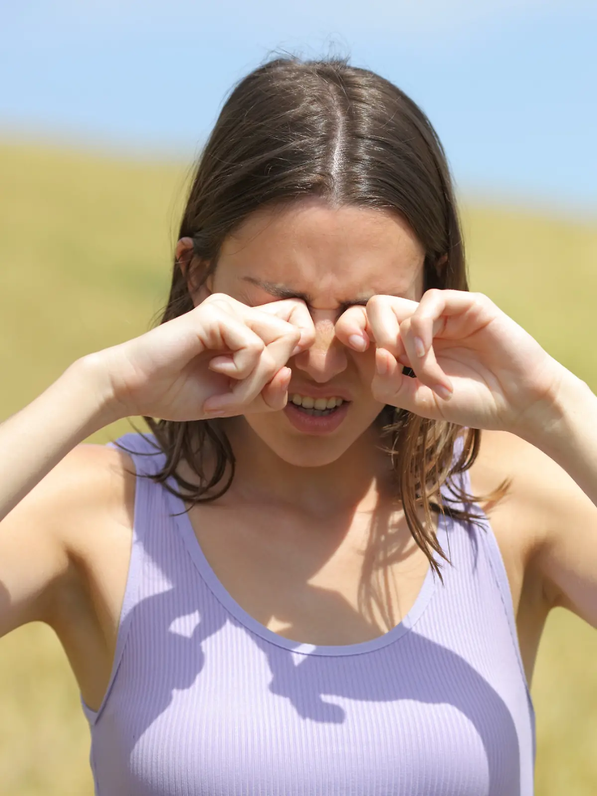 Eine Frau reibt sich im Sommer in einem Feld die Augen