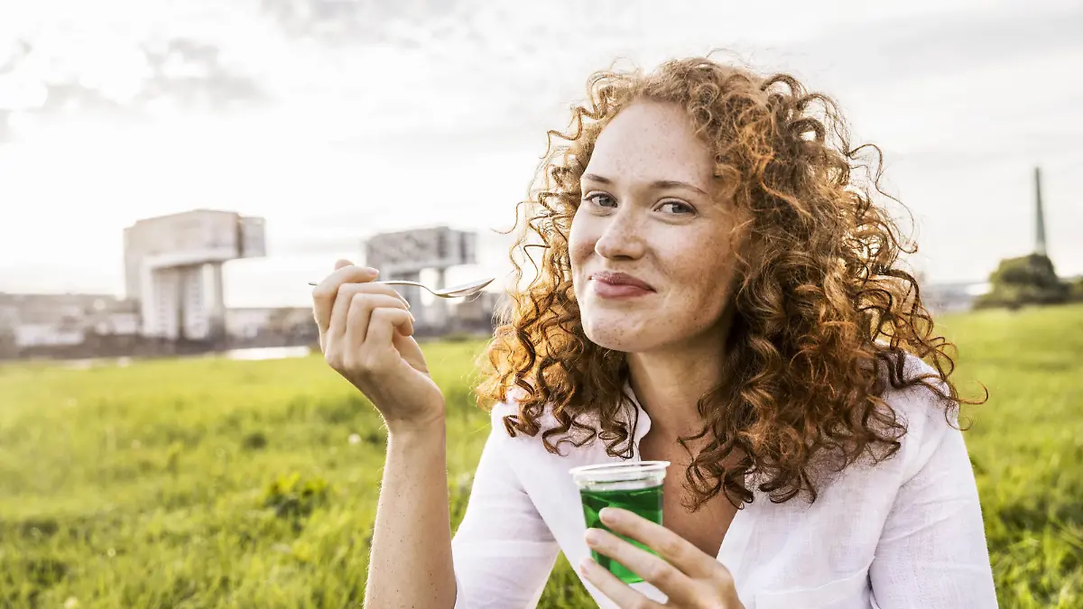 Germany, Cologne, portrait of happy young woman eating jelly on meadow model released Symbolfoto PUBLICATIONxINxGERxSUIxAUTxHUNxONLY FMKF04387