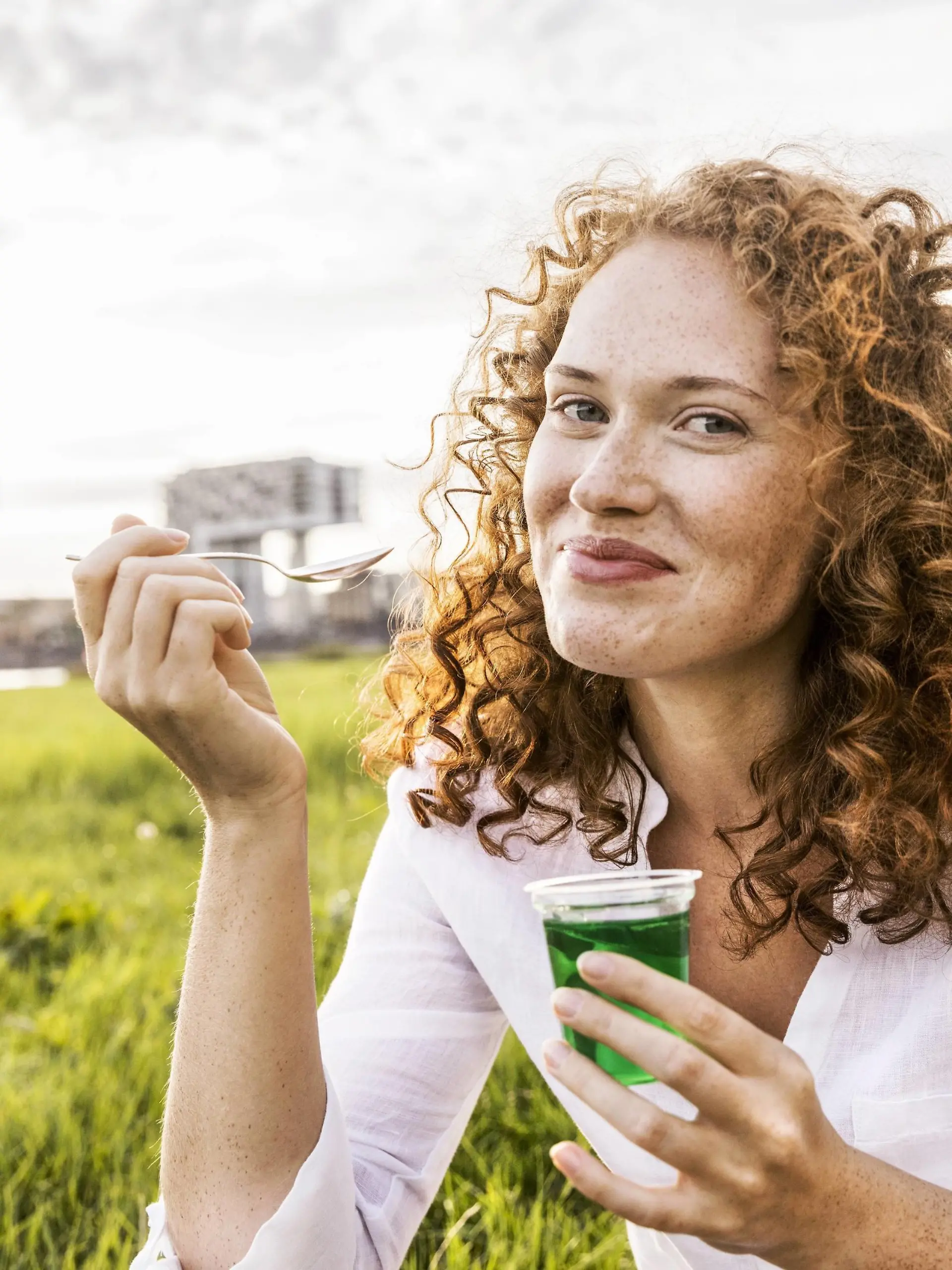 Germany, Cologne, portrait of happy young woman eating jelly on meadow model released Symbolfoto PUBLICATIONxINxGERxSUIxAUTxHUNxONLY FMKF04387