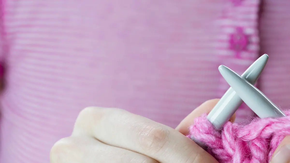 Close up of a female hands knitting pink woolen threads
