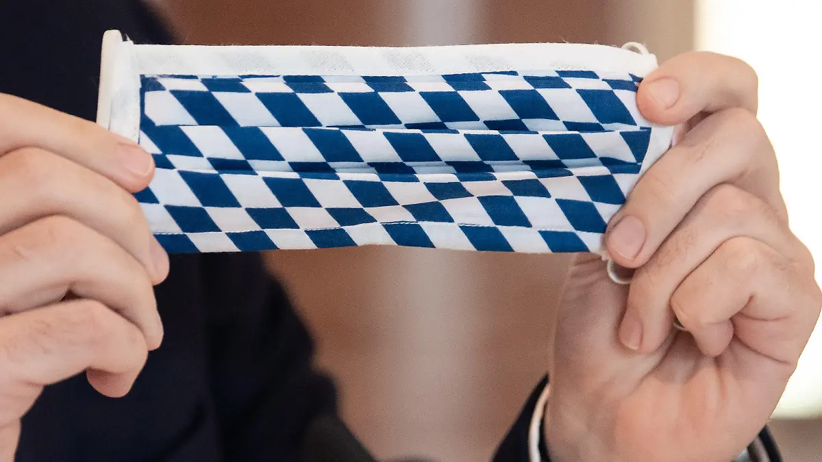16.04.2020, Bayern, München: Markus Söder (CSU), Ministerpräsident von Bayern, nimmt an einer Sitzung des bayerischen Kabinetts teil und hält dabei einen Mundschutz mit der bayerische Rautenflagge in den Händen. Um mehr Abstand voneinander einhalten zu können, findet die Kabinettssitzung im großen Kuppelsaal der bayerischen Staatskanzlei statt. Schwerpunkt der Sitzung ist die Corona-Krise. Foto: Sven Hoppe/dpa +++ dpa-Bildfunk +++