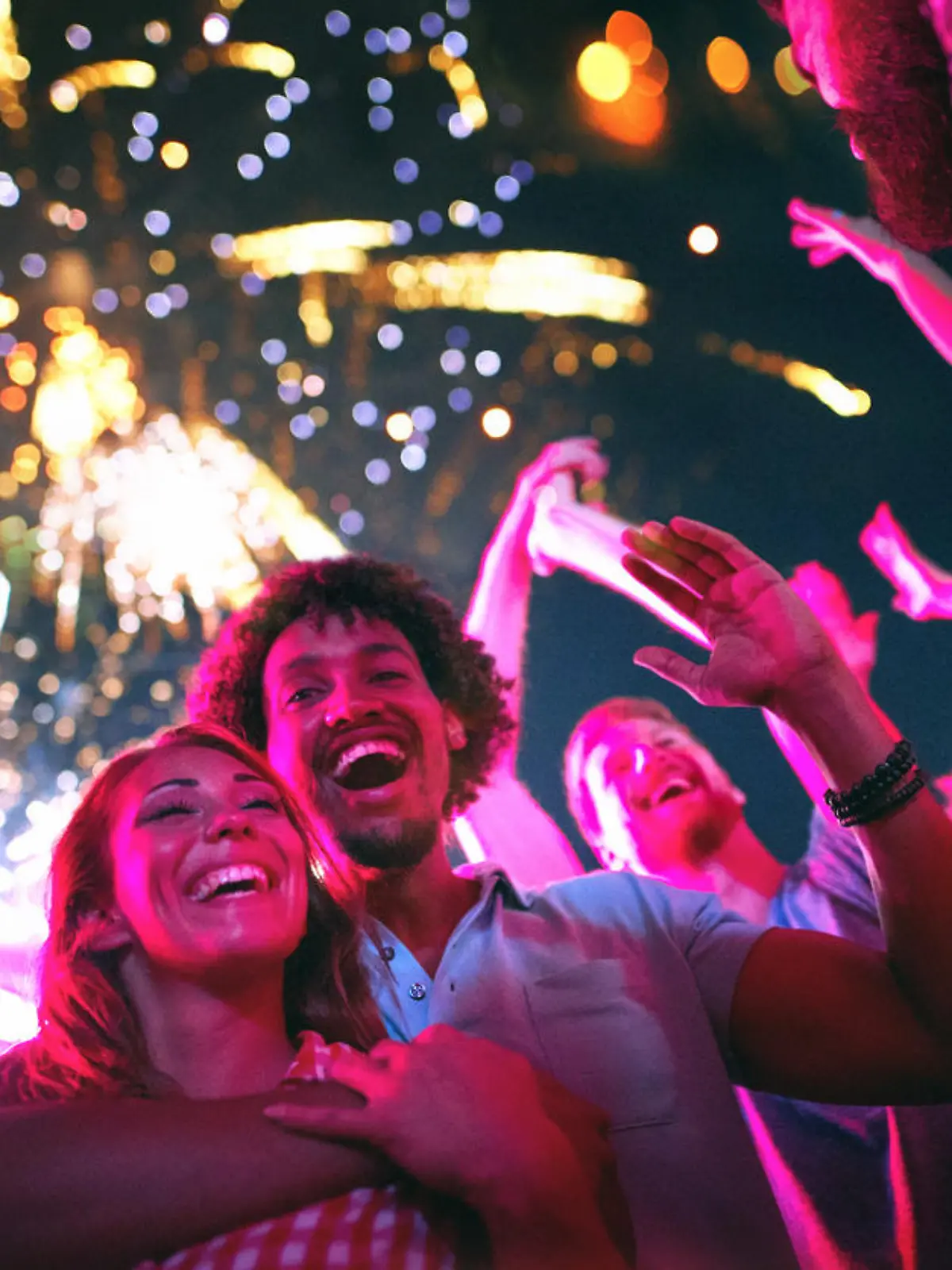 Closeup low angle view of group of multi ethnic young adults dancing and enjoying an open air concert on a summer afternoon. They are standing in a circle while fireworks popping in the background.